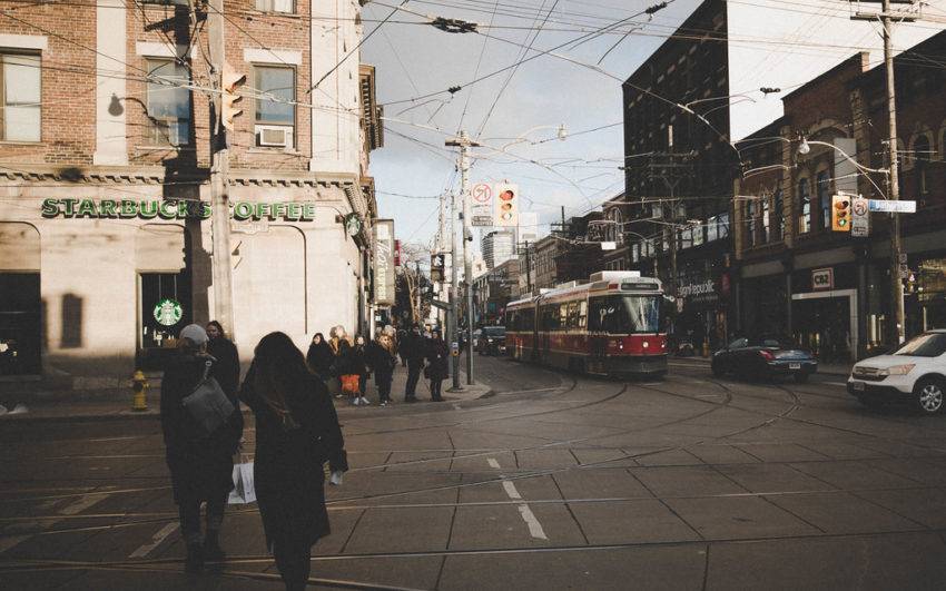 Pedestrians crossing street in front of Starbucks and red TTC streetcar.