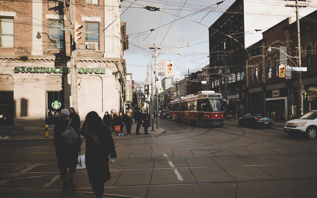 Pedestrians crossing street with Starbucks and red TTC streetcar in background.