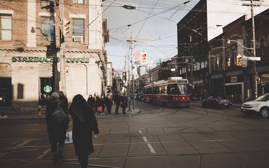 Pedestrians crossing street in front of Starbucks and red TTC streetcar.