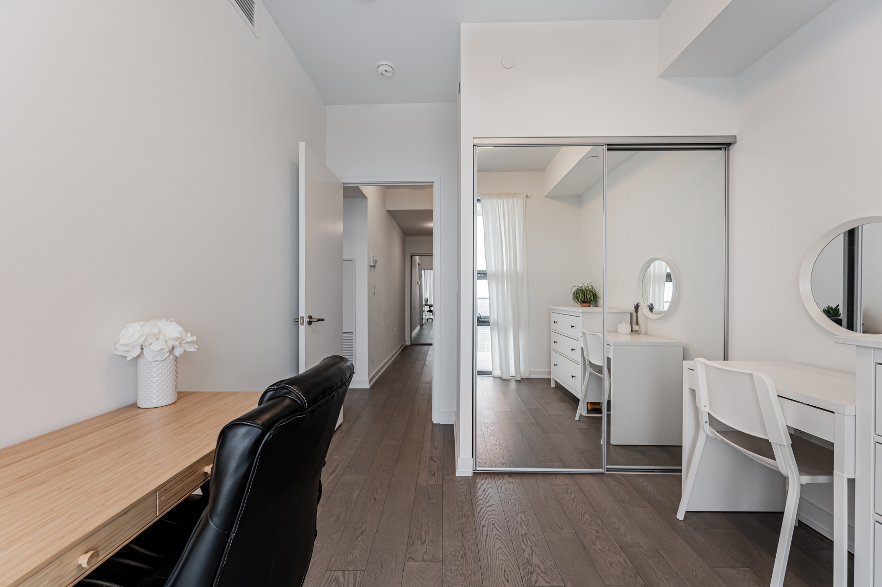 Condo bedroom with hardwood floors and mirror door closet.