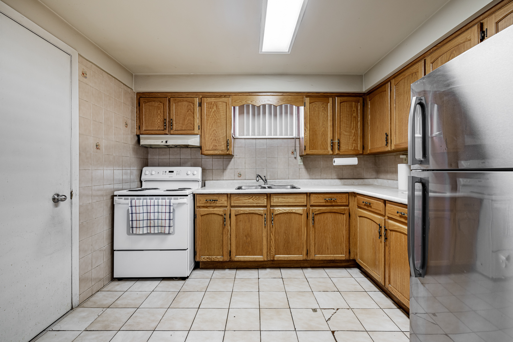 Basement kitchen with many cabinets, ceramic floors, tiled back-splash, fluorescent lighting and appliances.