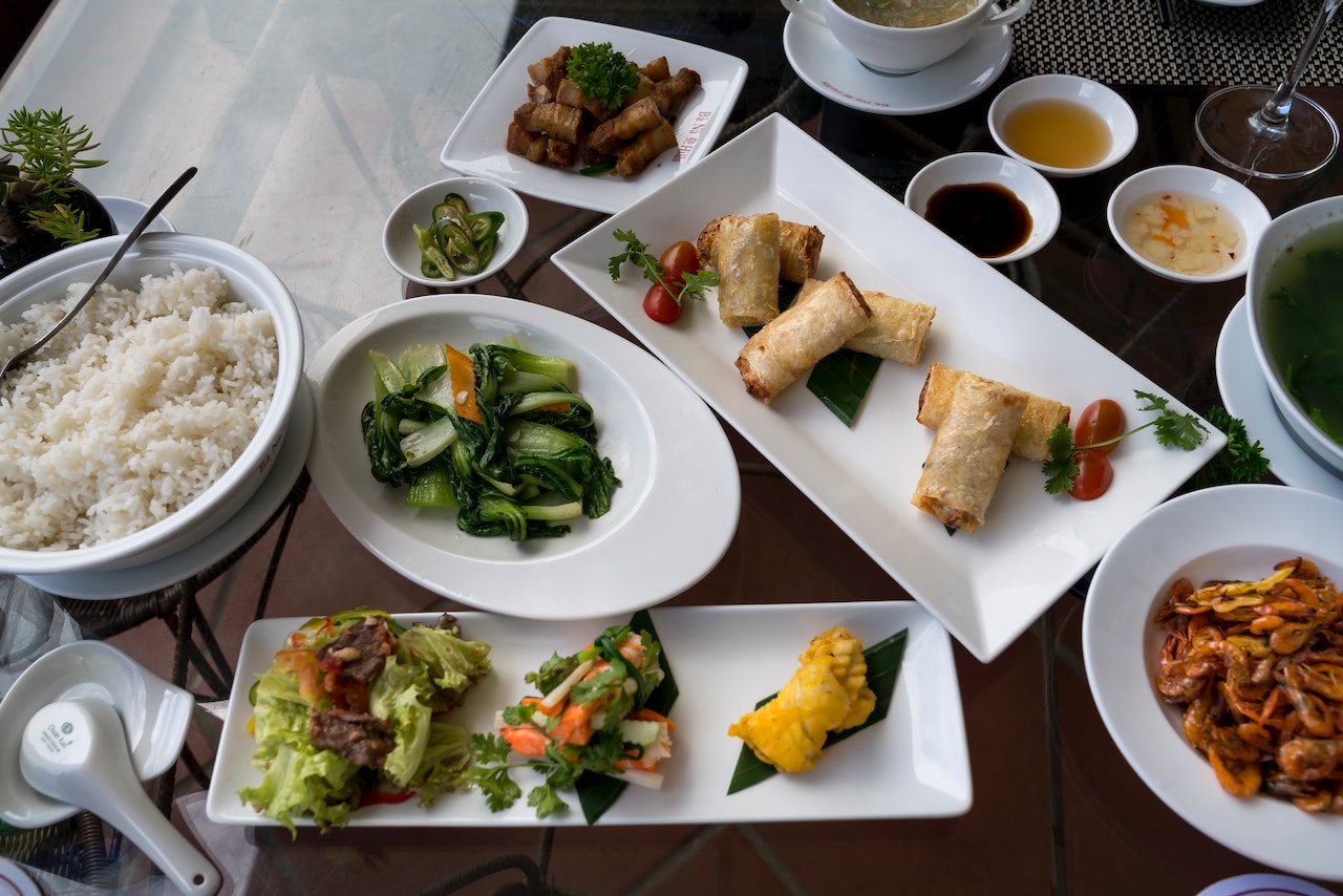 Table loaded with Chinese food in plates and bowls, including rice, vegetables and curry.