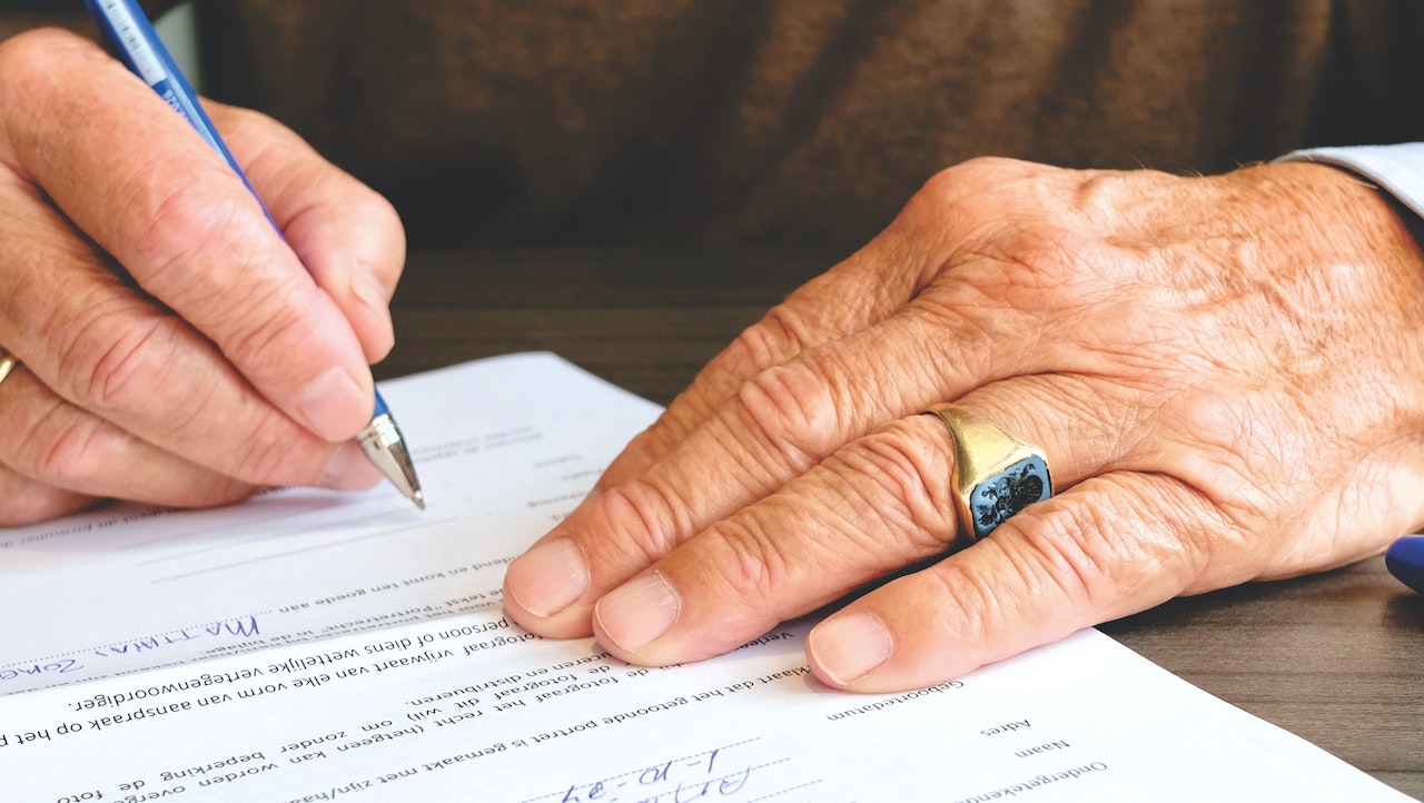 Close up of old man's hand signing document.