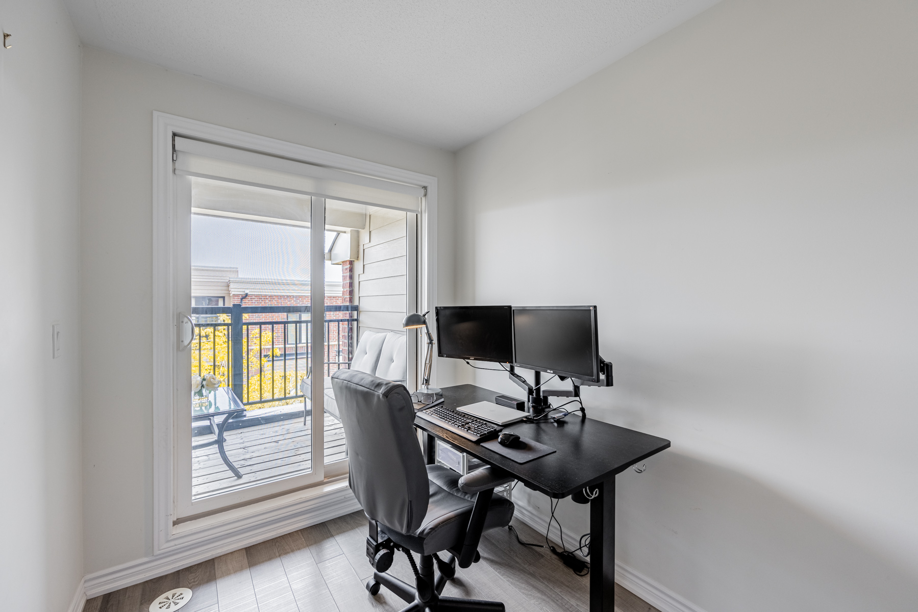 Townhouse bedroom with home office desk, chair and monitors with view of balcony.