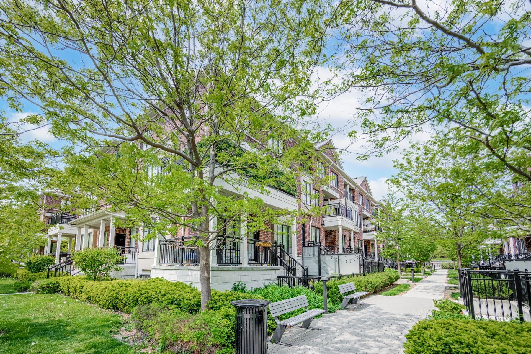 Row of townhouses with trees, bushes and benches.