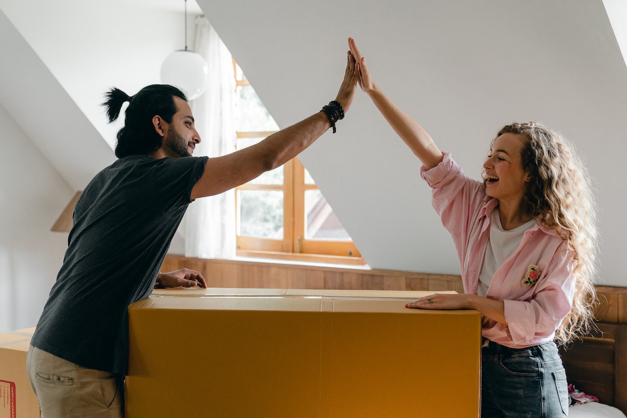 Young couple high-fiving over cardboard box in new home.