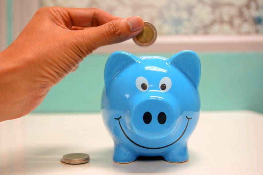 Hand putting coin into blue piggybank to show FHSA savings.