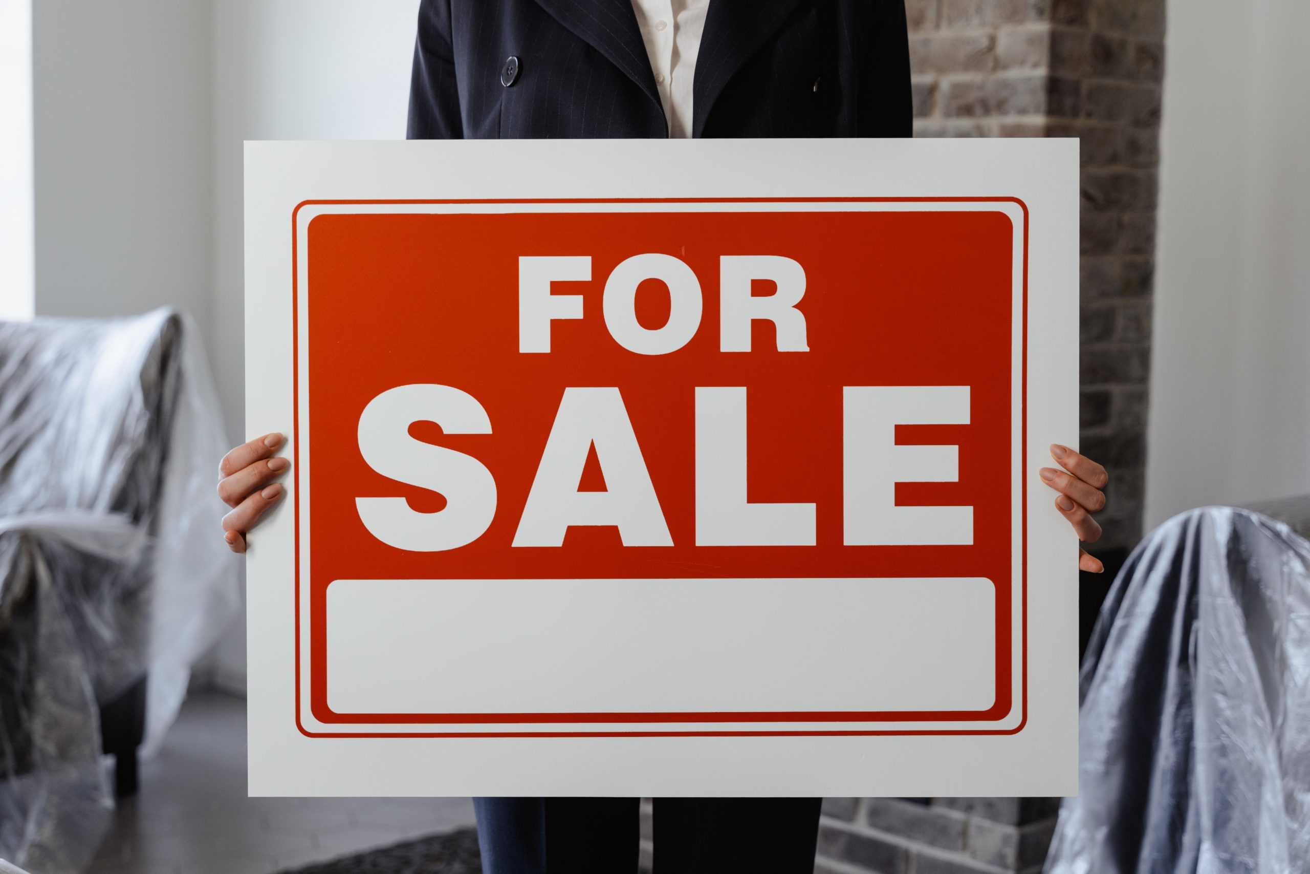 Woman in suit holding large For Sale sign.