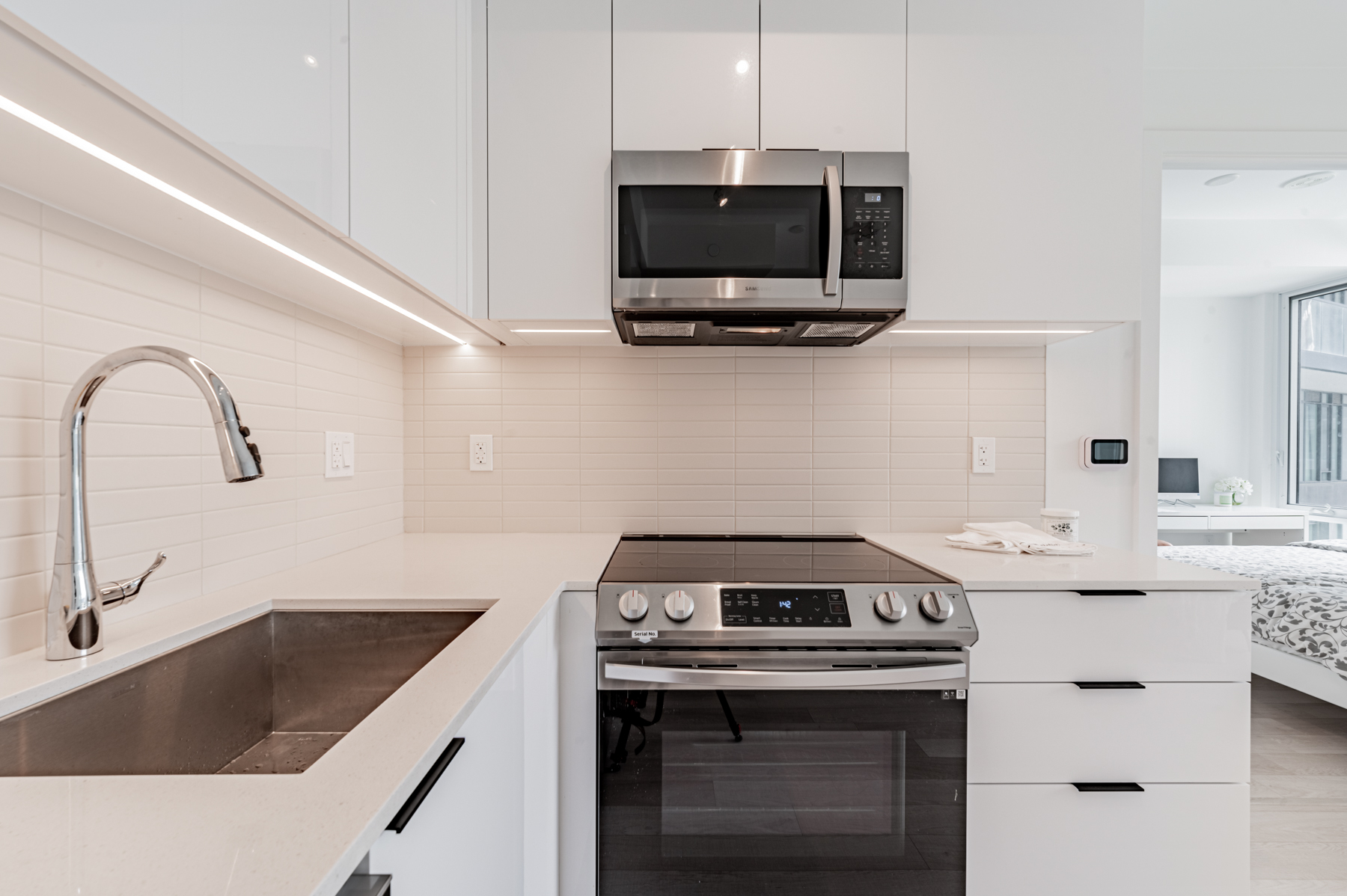 50 Power St Unit 618 kitchen with white counters, under-cabinet strip lighting and tiled back-splash.