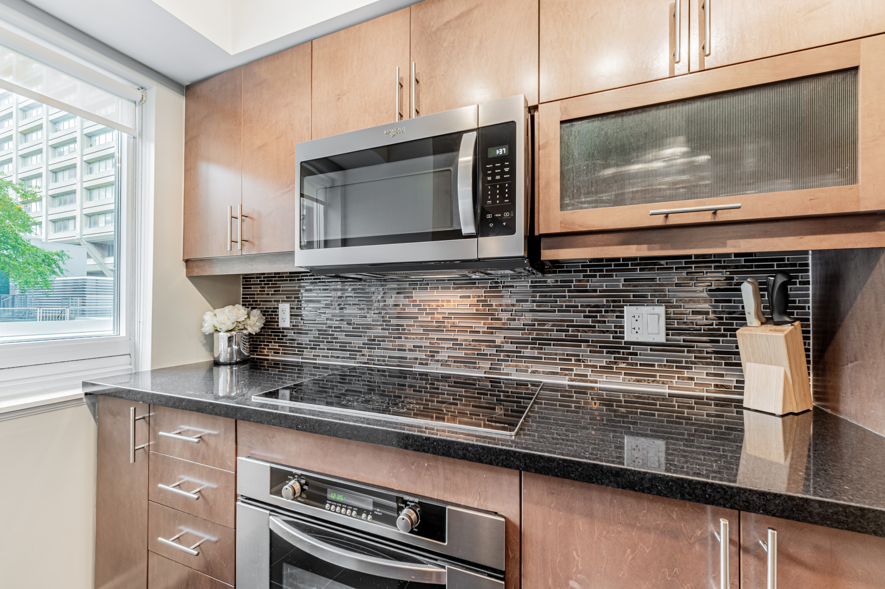 Closer view of kitchen's wood cabinets, ceramic back-splash and quartz counter-tops.
