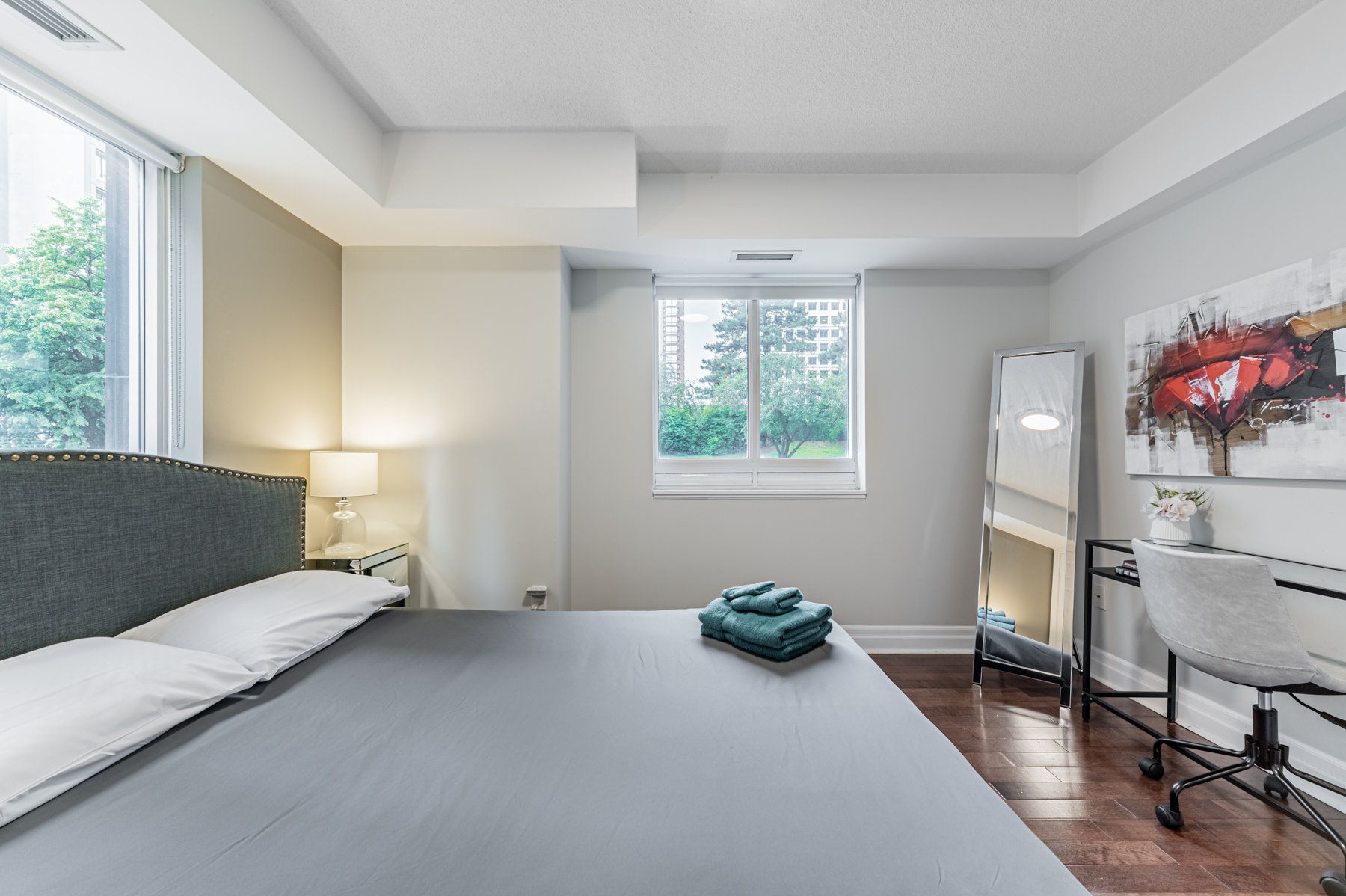 Condo bedroom with bed, nightstands and full-length mirror.