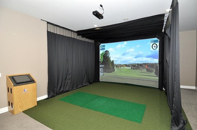 Golf simulator with green surface, large screen and black curtains.