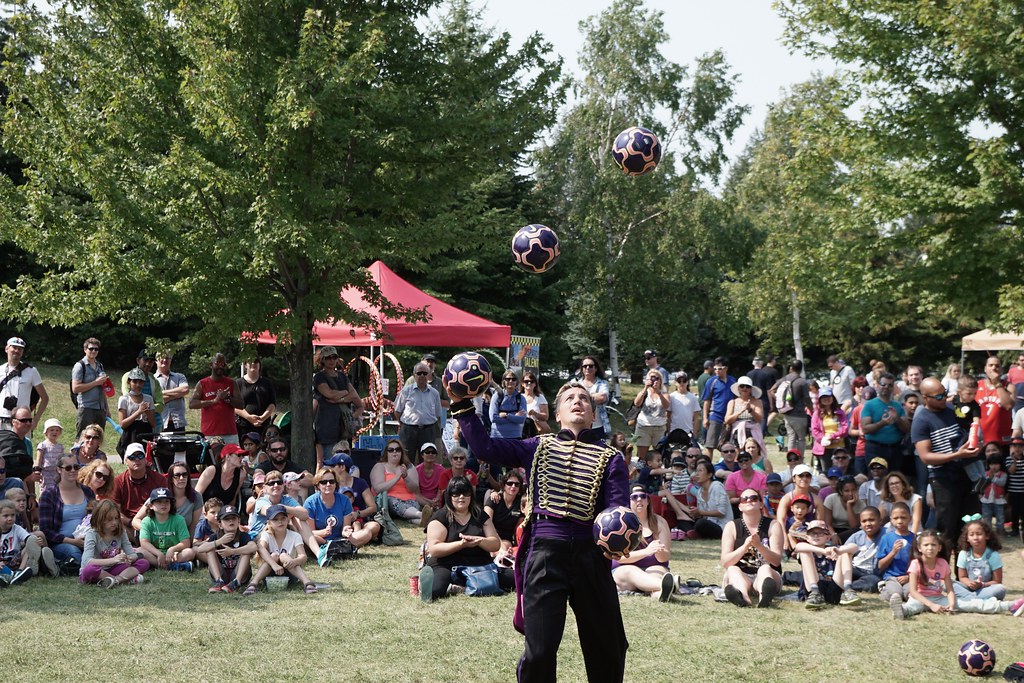 Busker juggling balls at park in Distillery District Toronto in front of crowd.