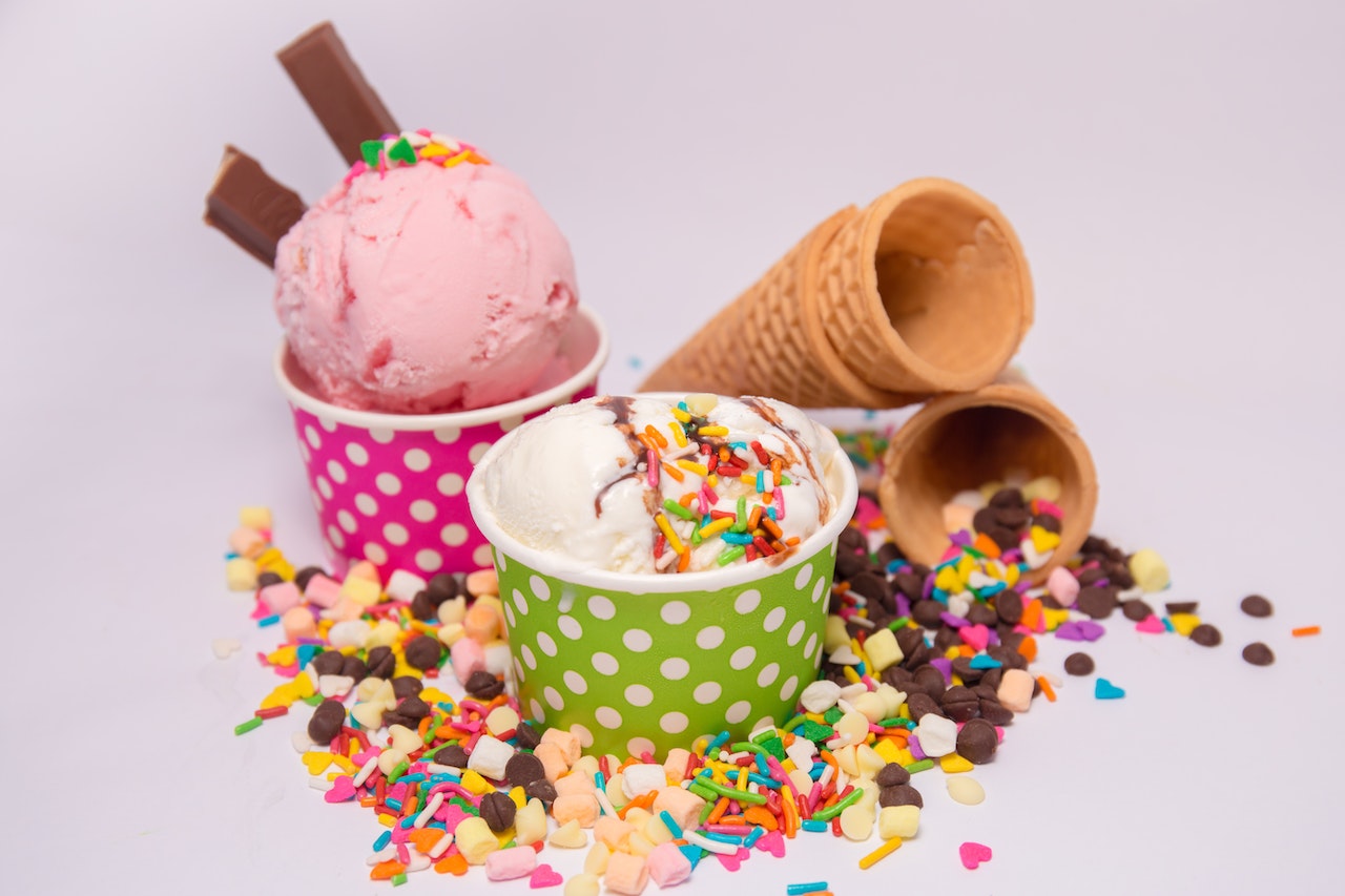 Ice cream in containers, cones, and colourful sprinkles.