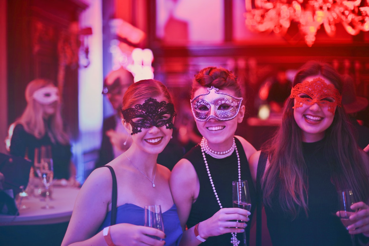 3 young women wearing masks and holding drinks in a bar.