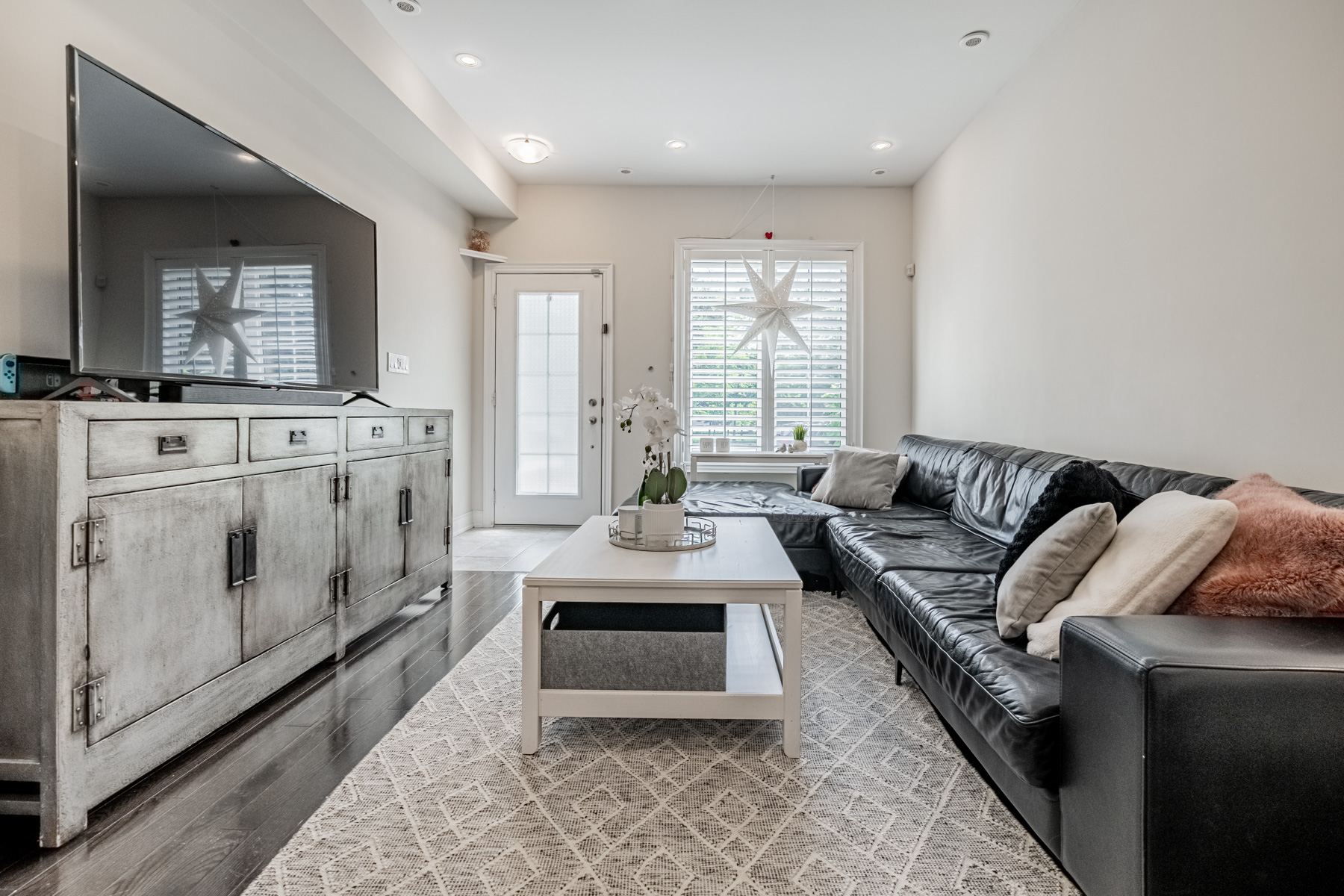 Condo living room lit by pot-lights, ceiling lamp and windows.