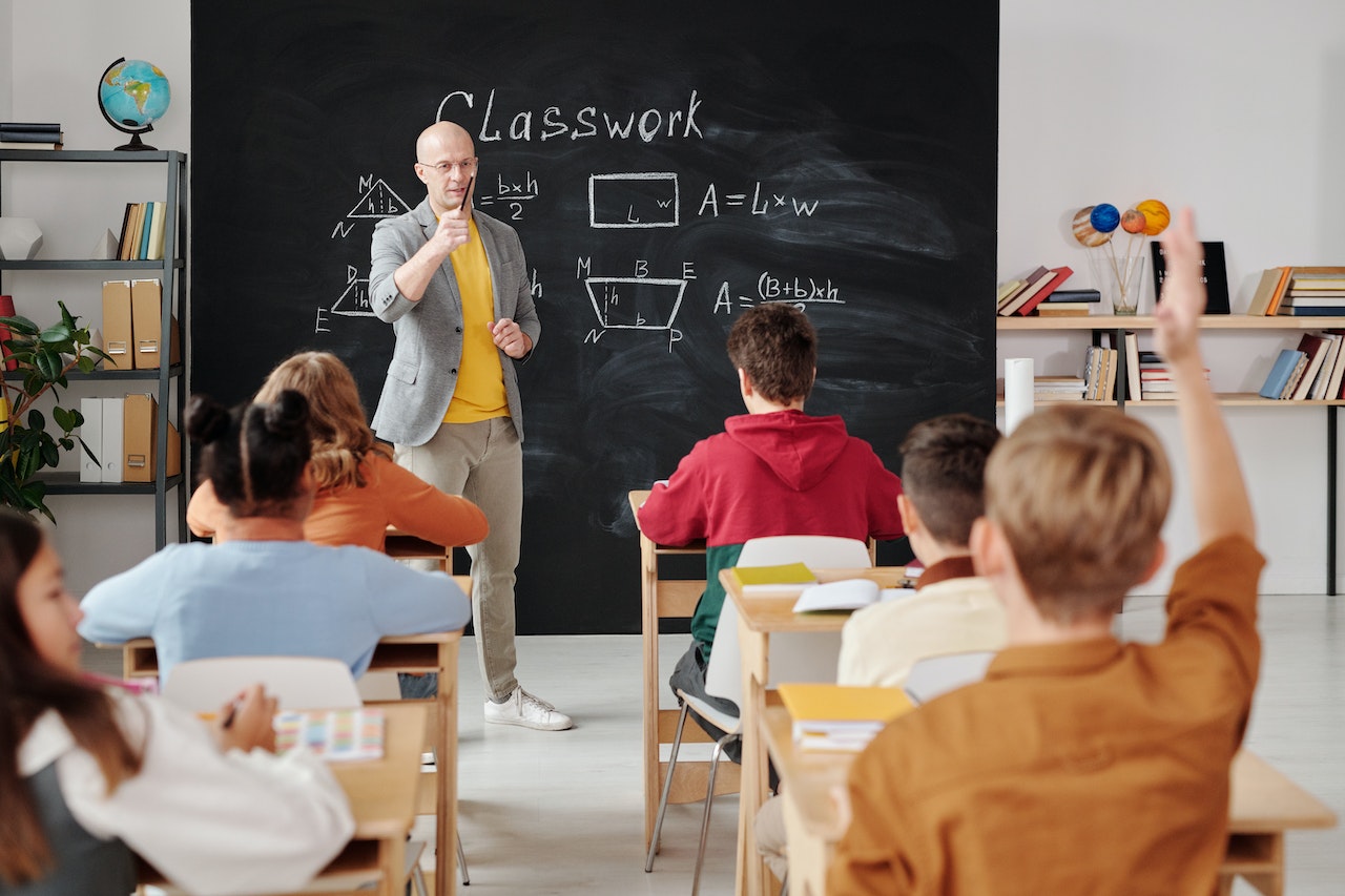 Teacher standing in front of blackboard with geometry problem with kids sitting at desk.