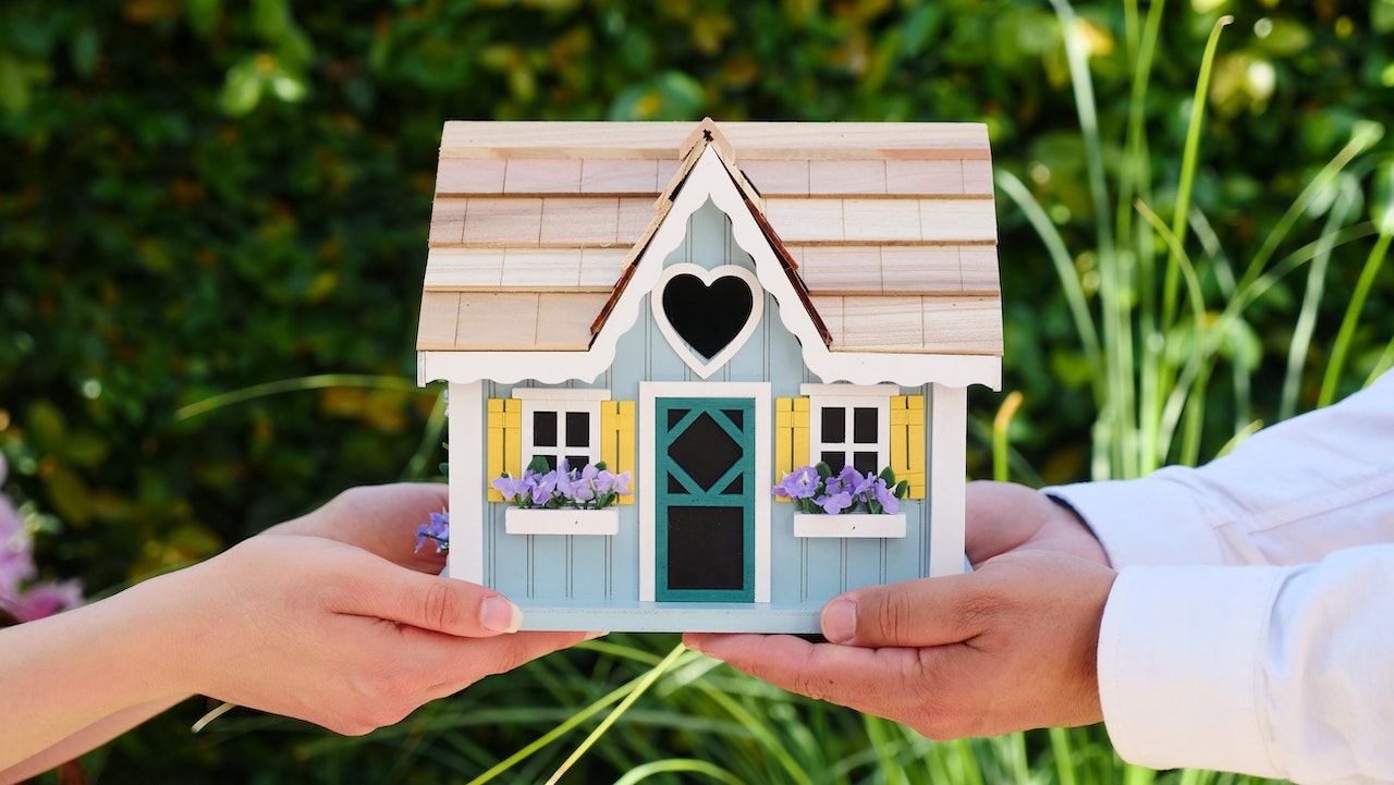 Two sets of hands holding up a bright toy house. 