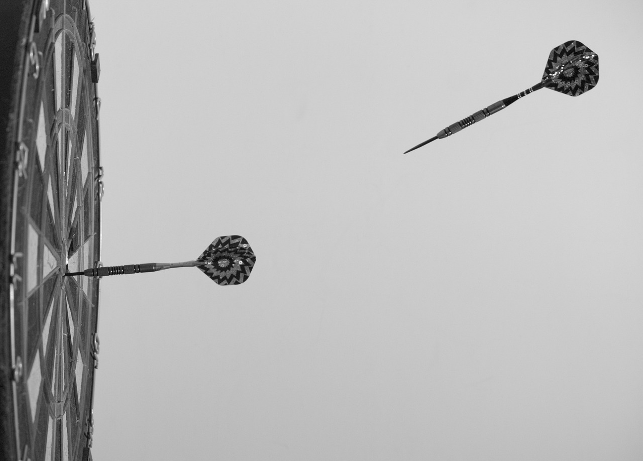 Black and white image of dart board and flying dart.