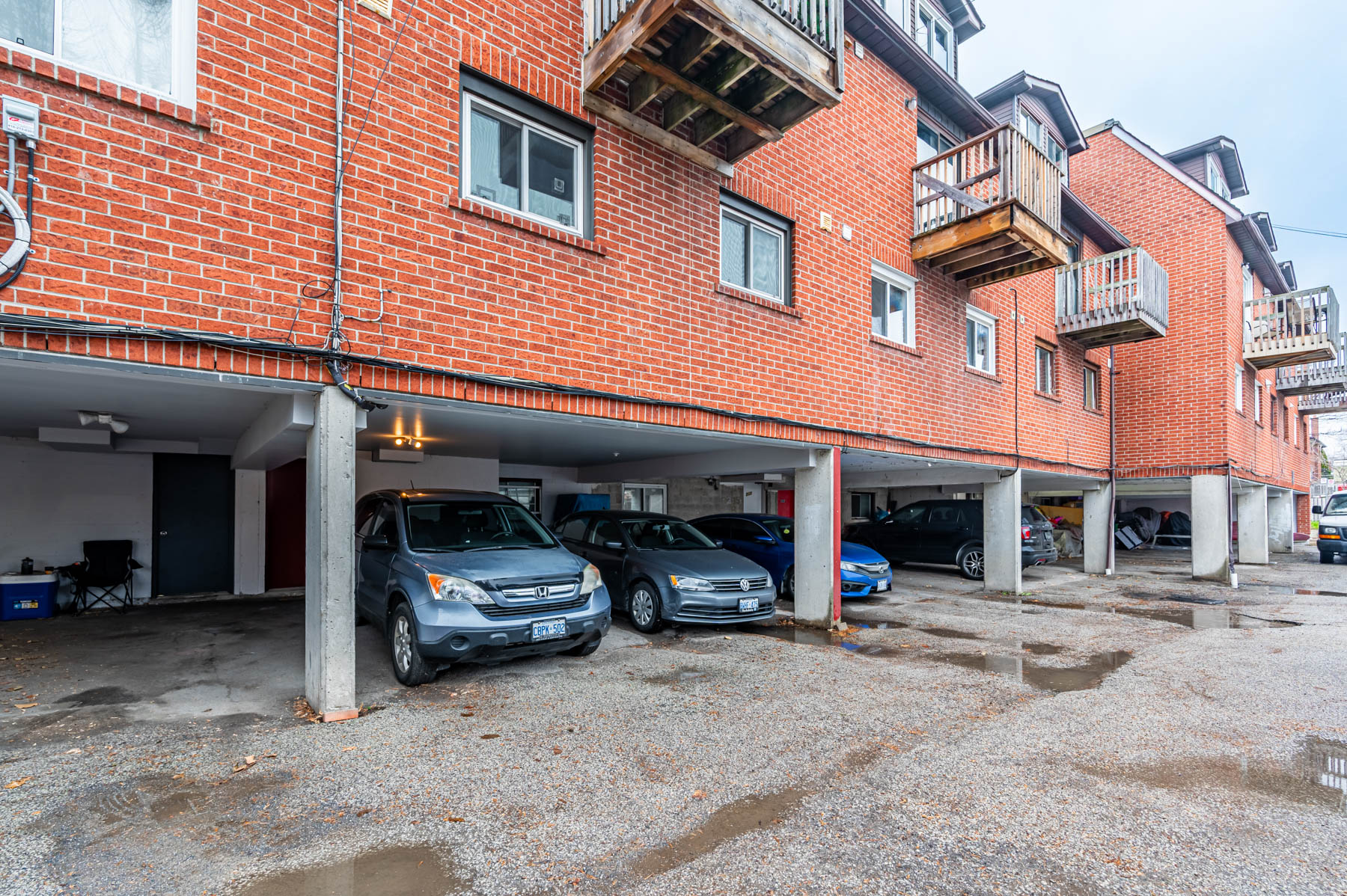 Red-brick building carport with vehicles parked below.