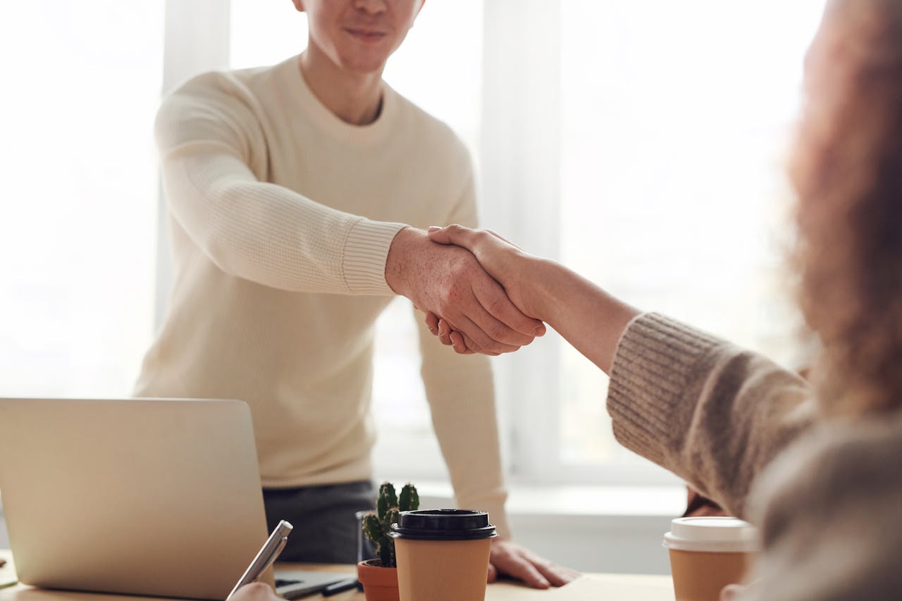 Man in white sweater shaking woman's hand to show client relationship.