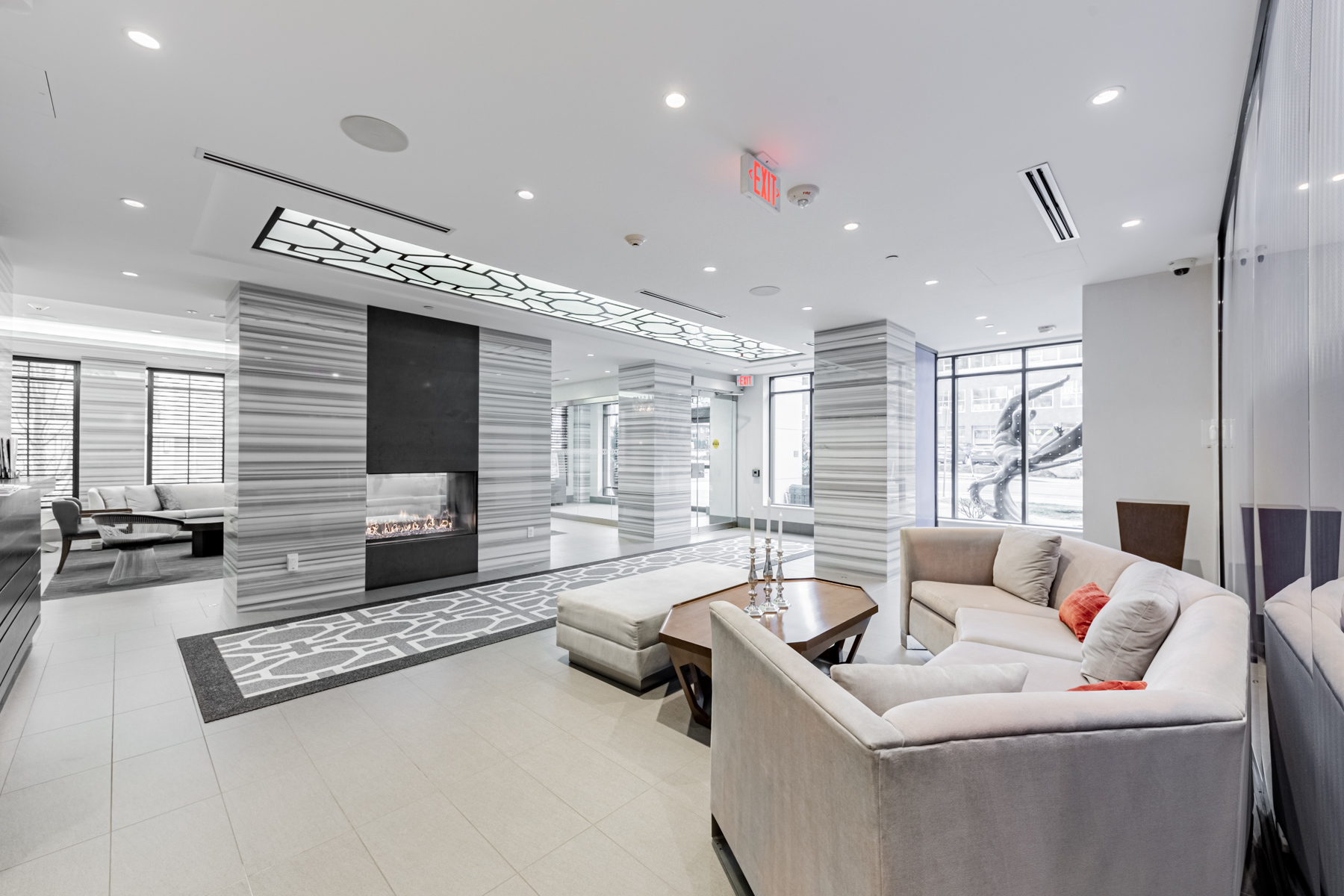 Condo lobby with gray walls, floors and ceiling, plus modern furniture and fireplace.