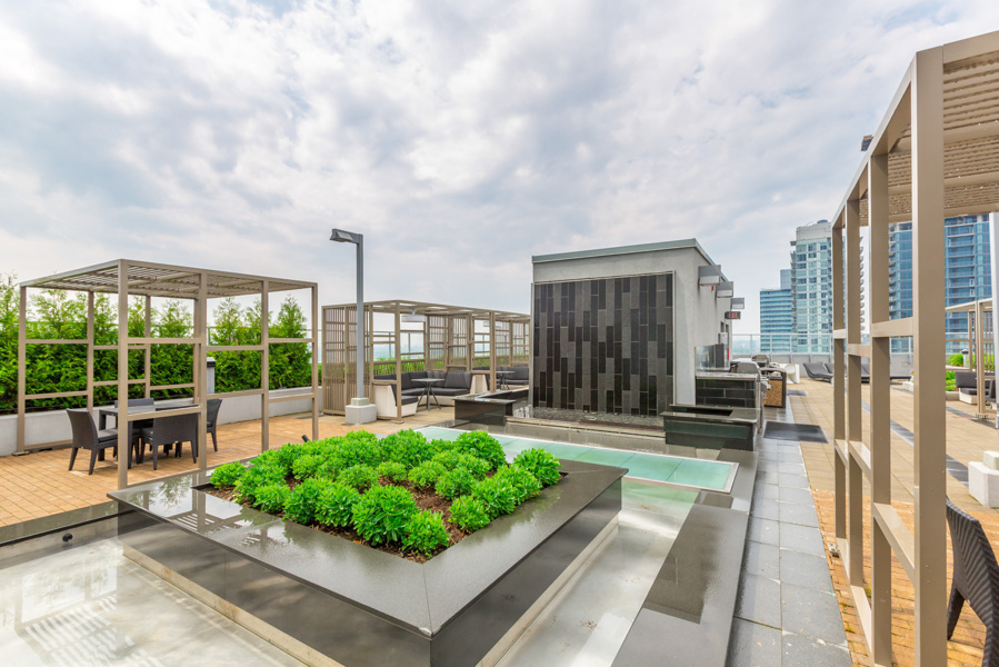 FLY Condos rooftop deck with cabanas, greenery, chairs, and city views.