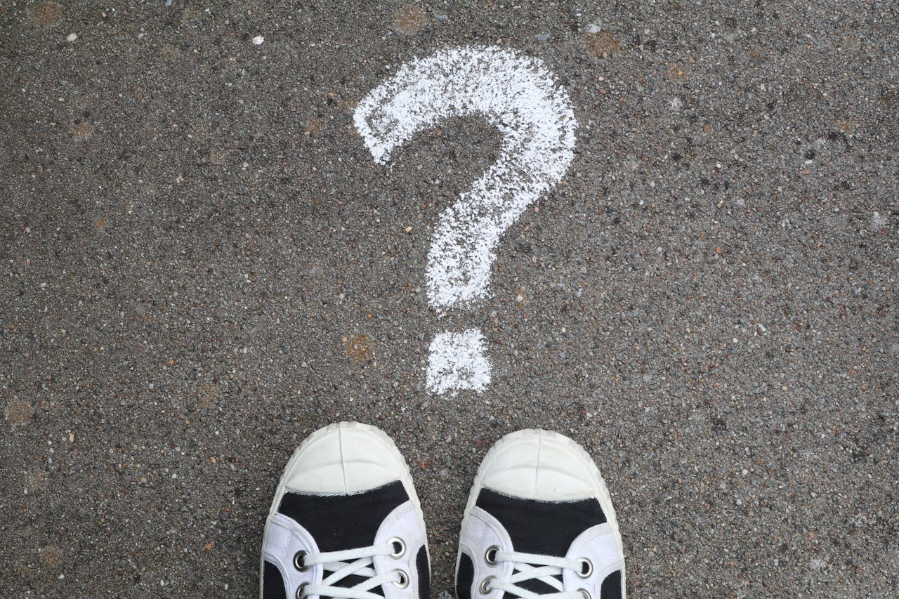 Chalk question mark on asphalt with sneakers to show buyer confusion. 