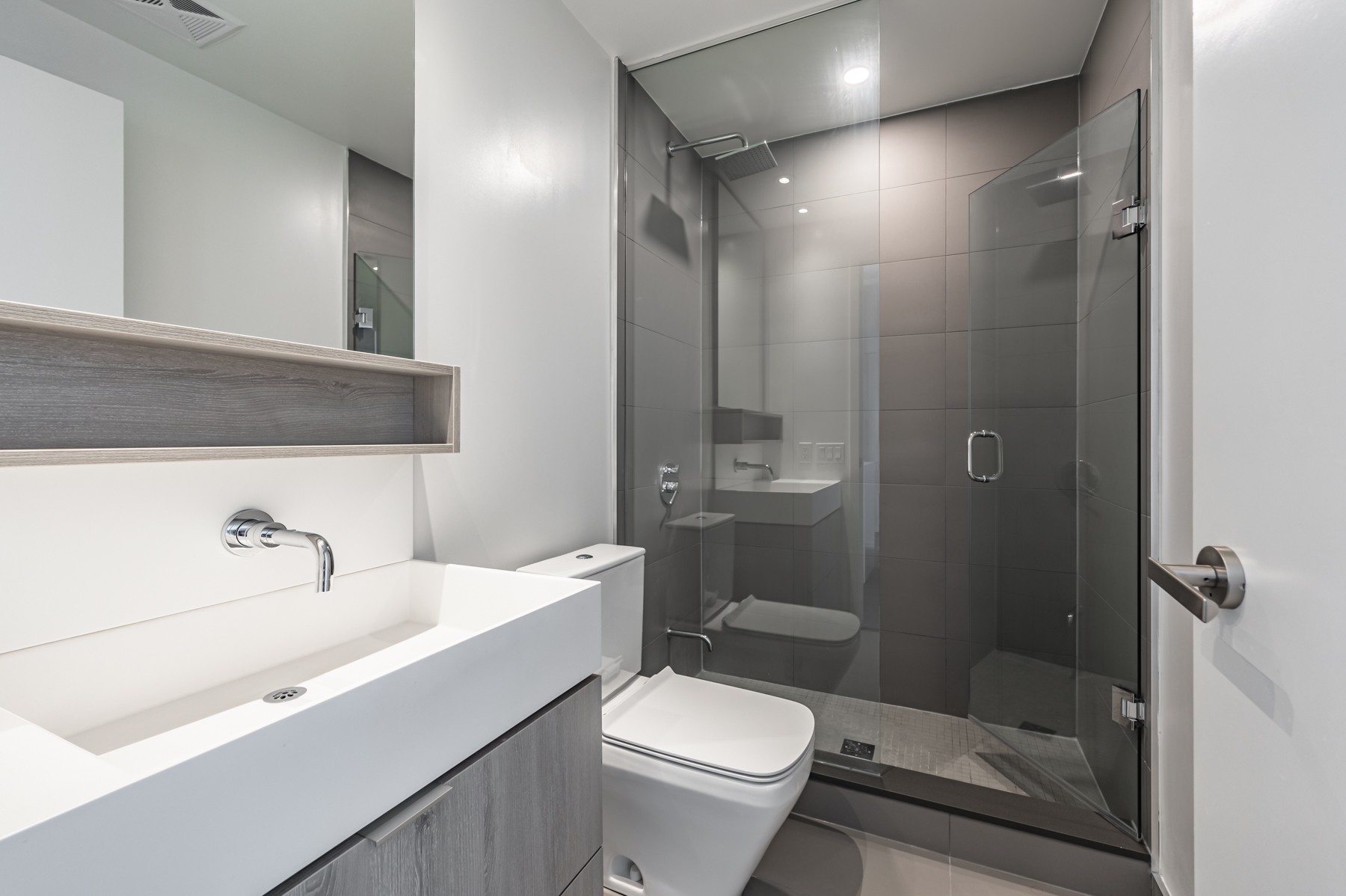 1702-5 Soudan Ave bathroom with frameless glass shower, dark tiles, shelves, wall-mounted faucet and ceramic tiles.