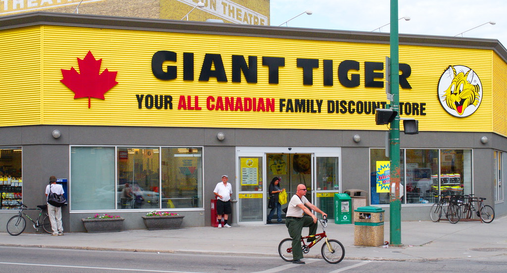 Yellow Giant Tiger storefront with pedestrians and cyclist in front.