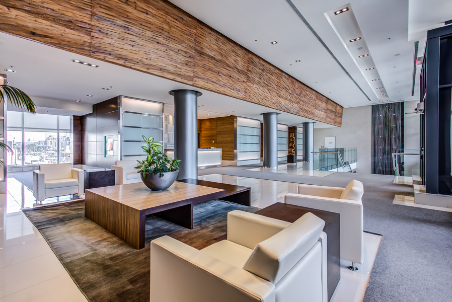 Condo lobby with wood-paneled ceilings, modern furniture, silver columns, and waterfall.