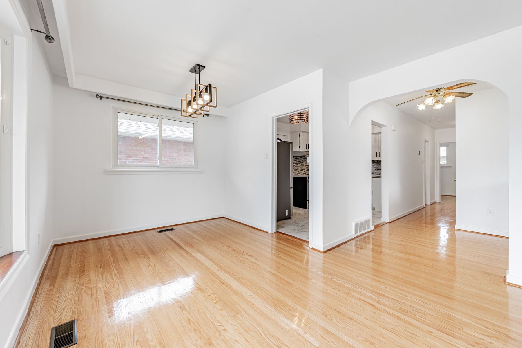 House living and dining room with gleaming hardwood floors and elegant light-fixtures.