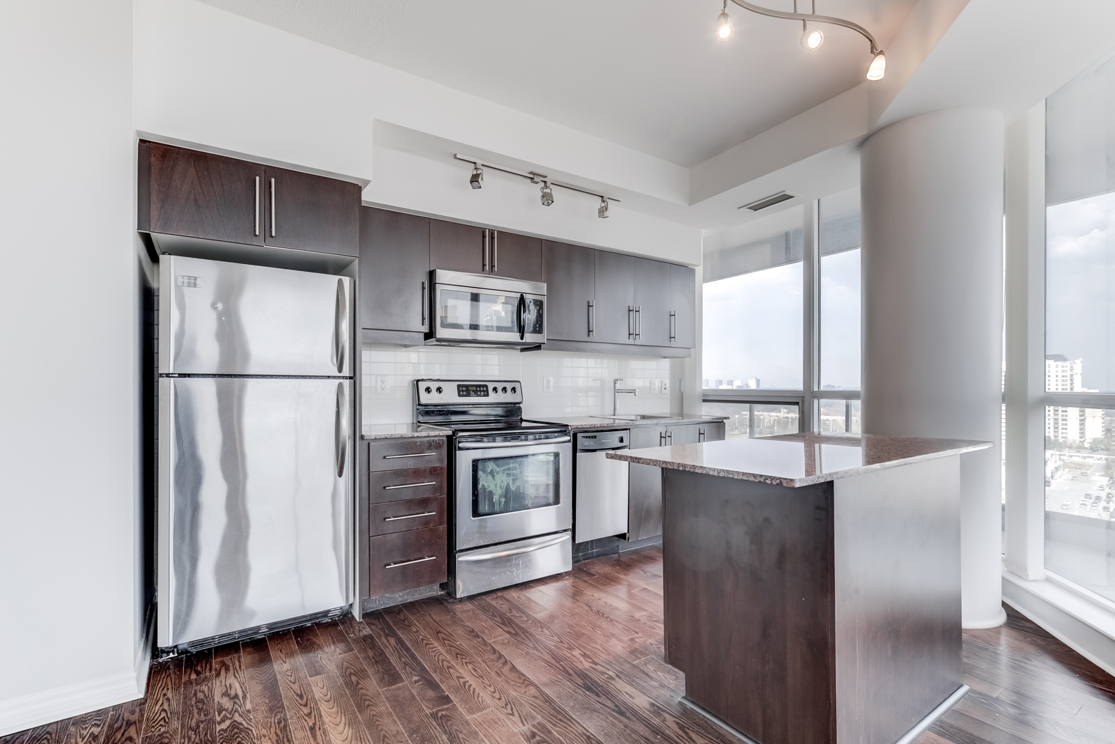 Linear condo kitchen with dark brown drawers, cabinets, stainless-steel appliances, tiled back-splash.