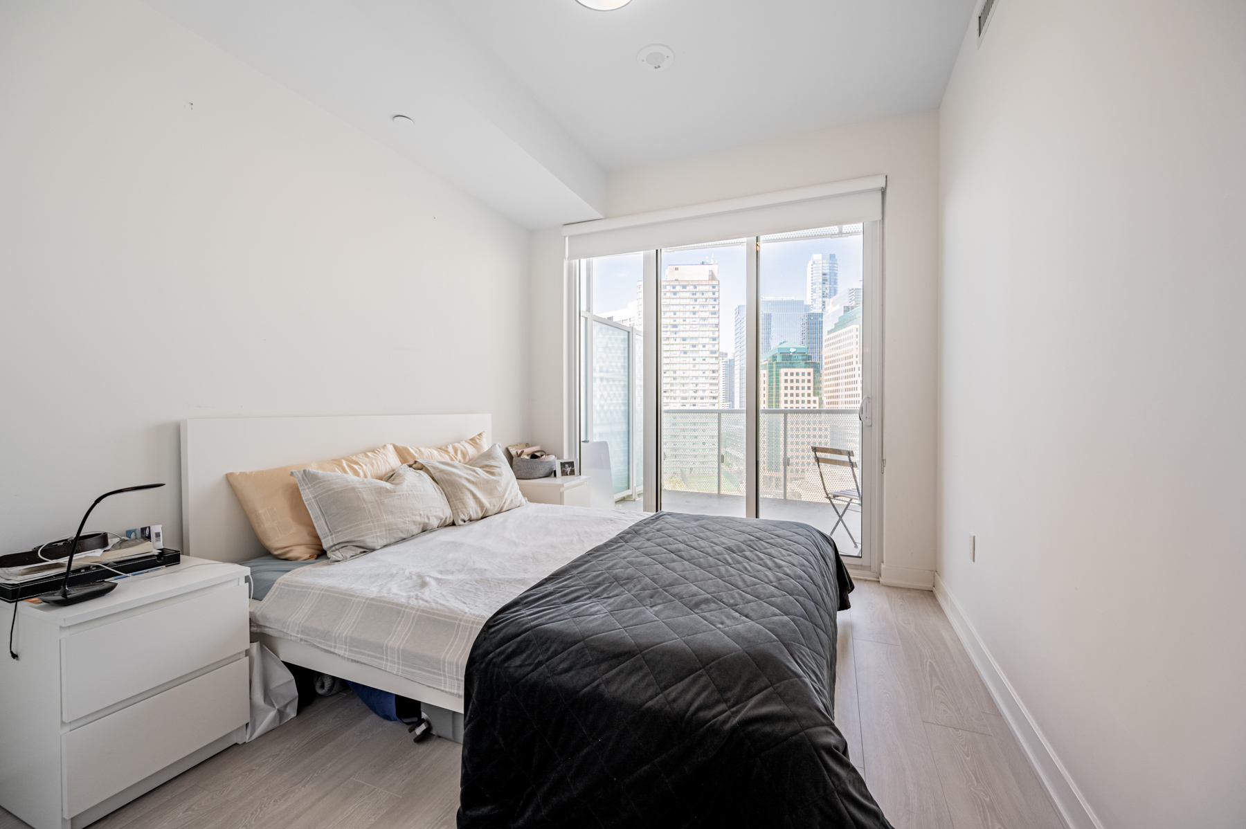 15 Queens Quay E Suite 1405 primary bedroom with light coloured walls, floors and city view from balcony doors.