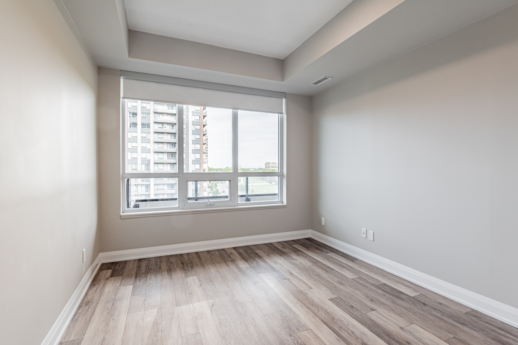 Condo bedroom with dark vinyl floors and large windows.