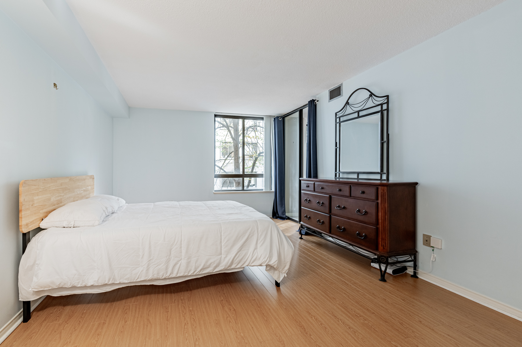 Large primary bedroom with laminate floors and bed – 280 Simcoe St 308A. 