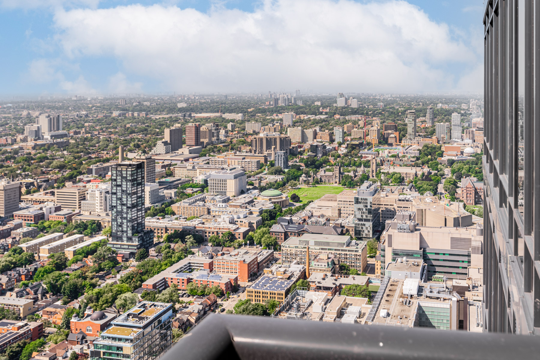 Balcony view of Toronto, including buildings, trees and blue skies.