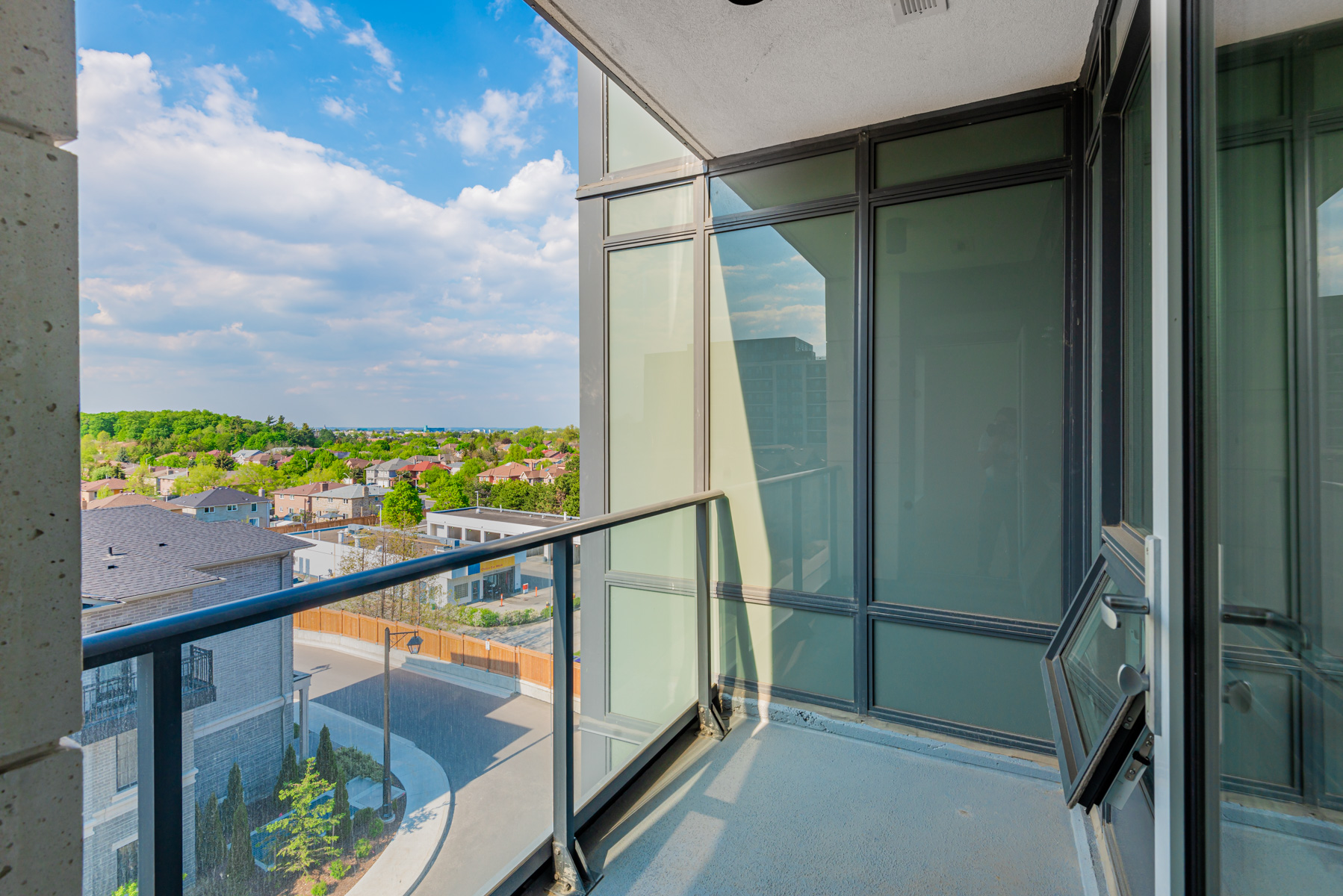 Condo balcony with glass panels and partial view of houses and trees.