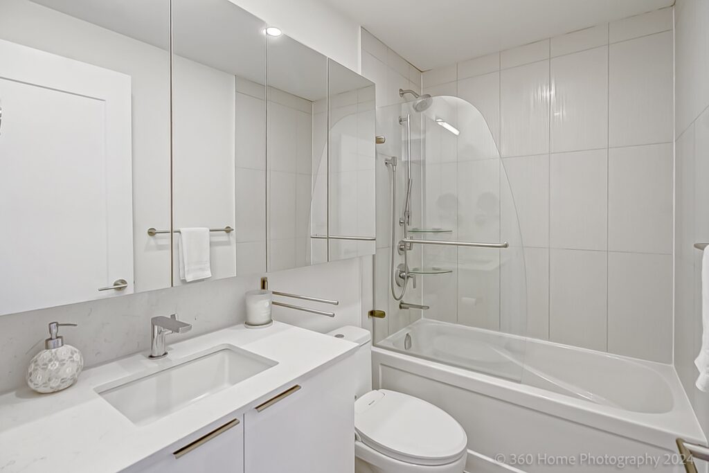 28 Freeland St Unit 2401 4-piece bath with quartz counters, ceramic tiles, and soaker tub with glass partition.