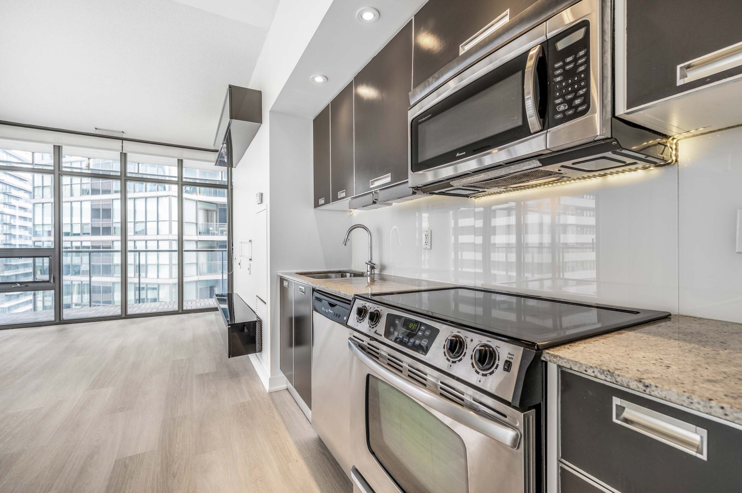 33 Charles St E Unit 3808 linear kitchen with granite counters, dark cabinets and white back-splash.