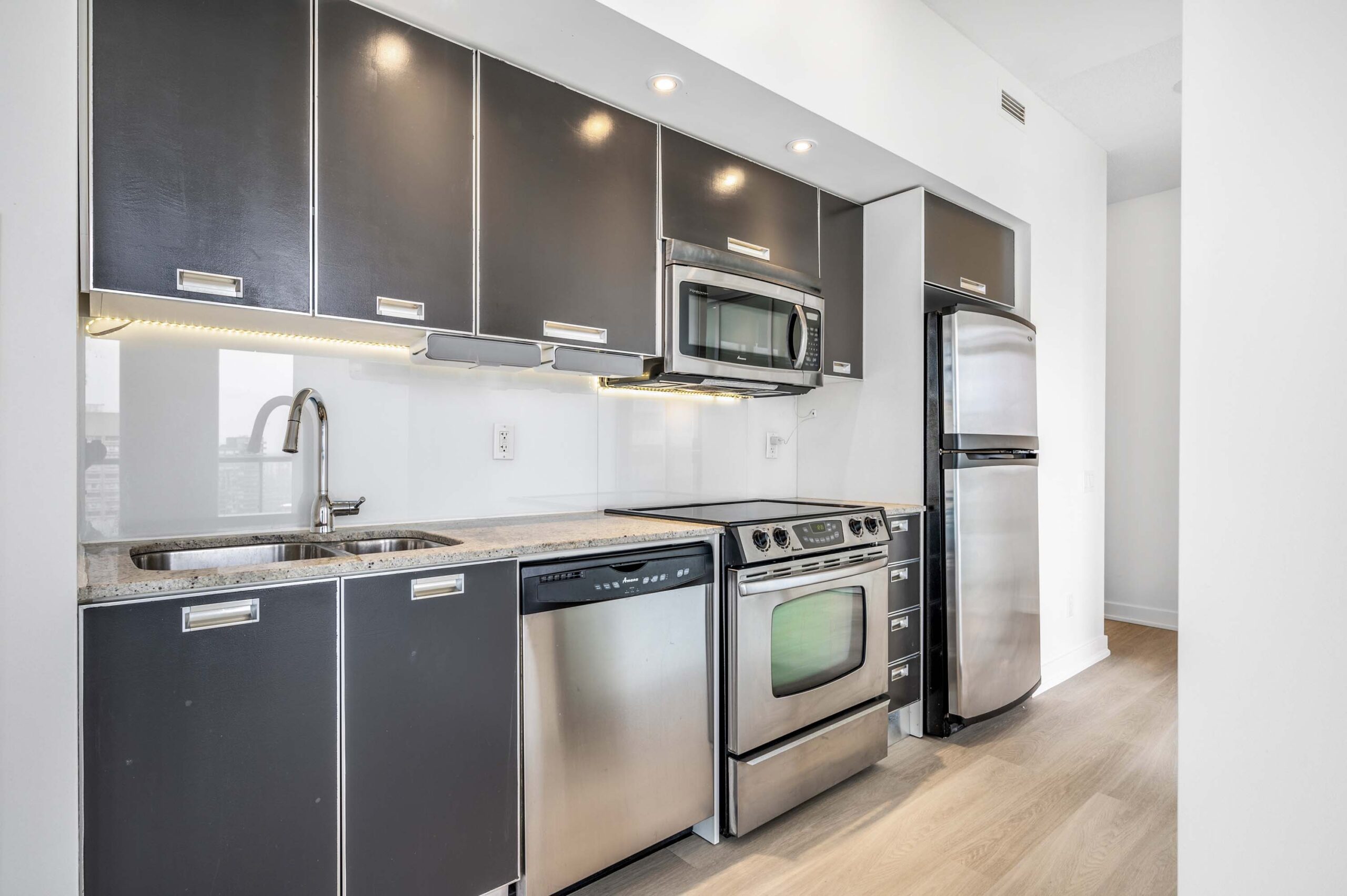 Condo kitchen lit by pot-lights, under-cabinet lights and natural sunlight.