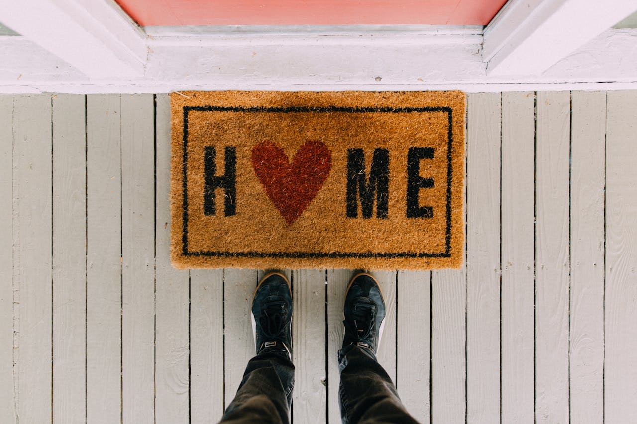 Looking down at welcome mat with word "HOME" heart in place of O.