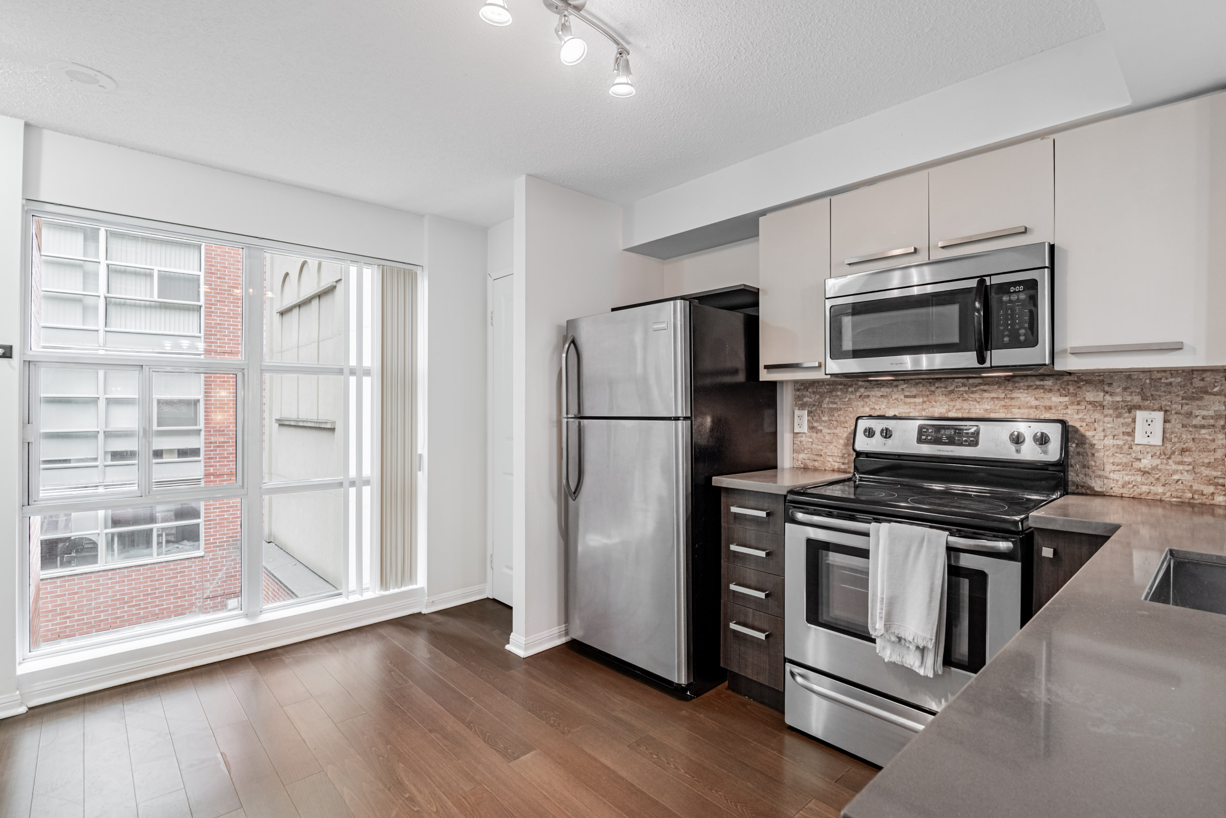 Condo kitchen with floor-to-ceiling windows showing view of building in distance.