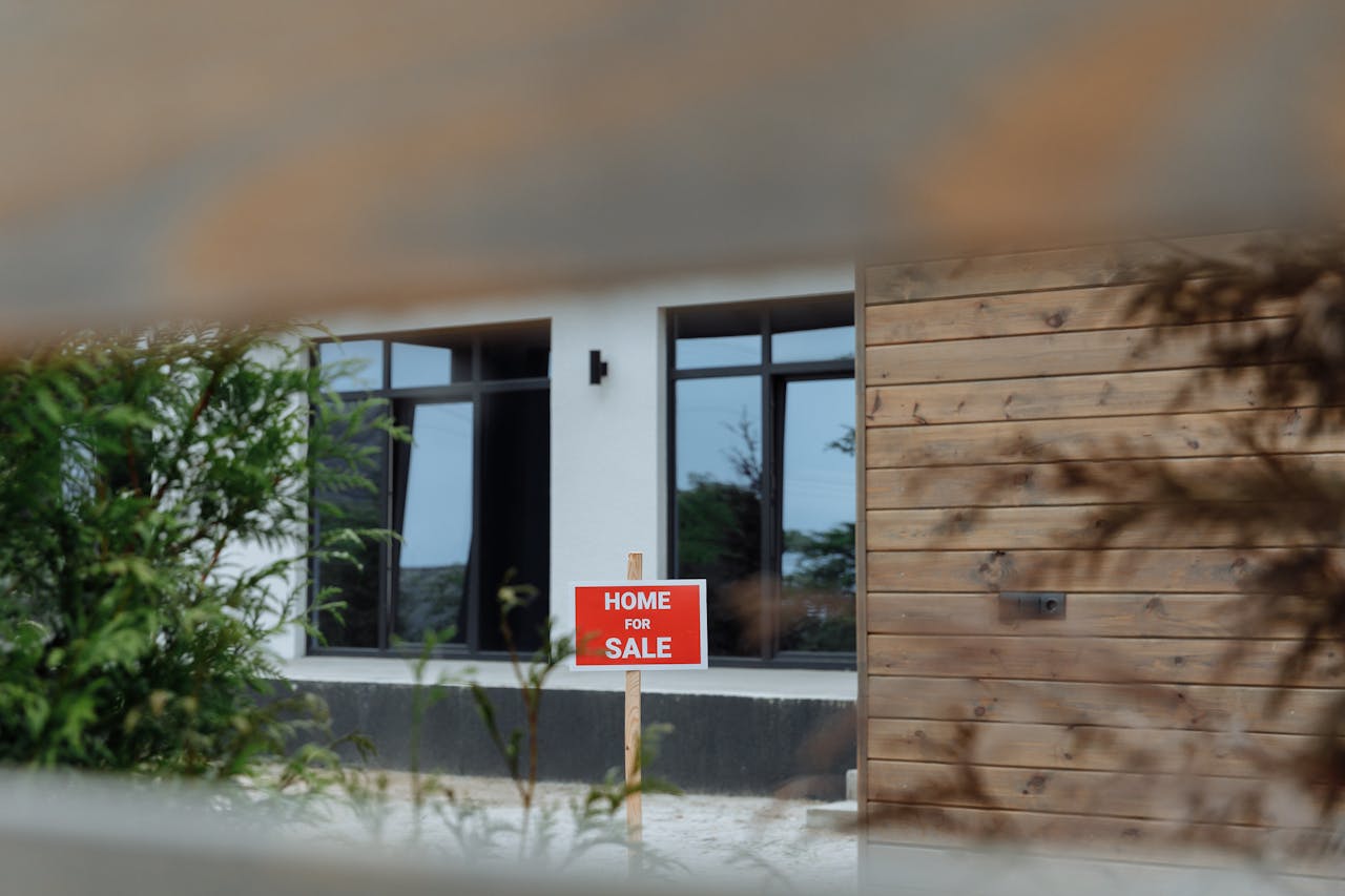 Photo of Home for Sale sign in front of suburban house, likely a bungalow.
