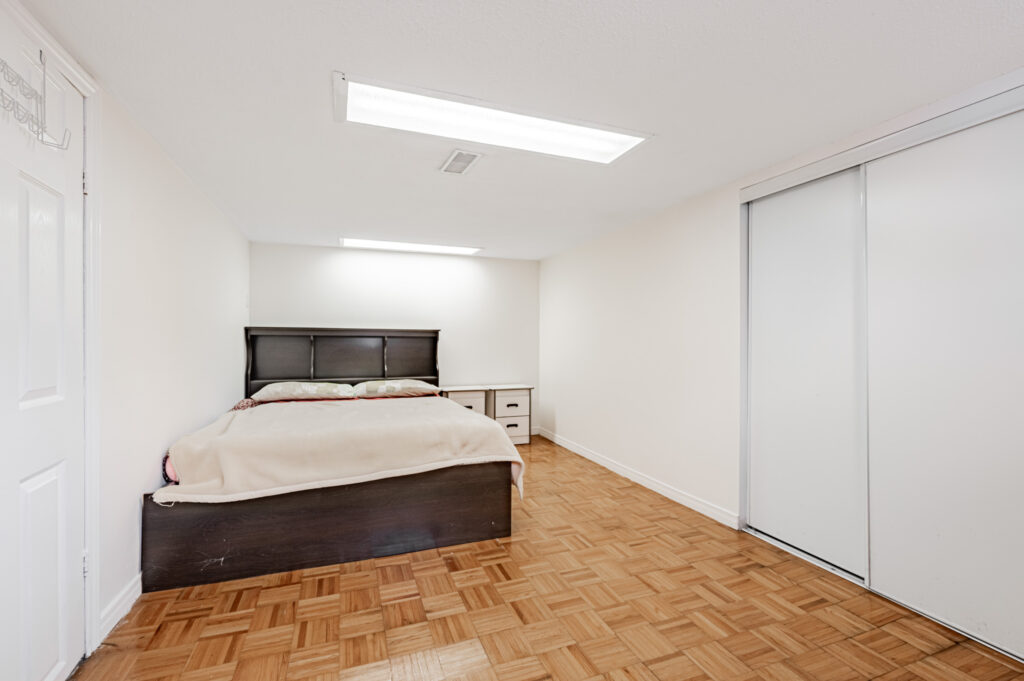 42 Carr St spacious basement bedroom with large bed, parquet floors and double-door closet.