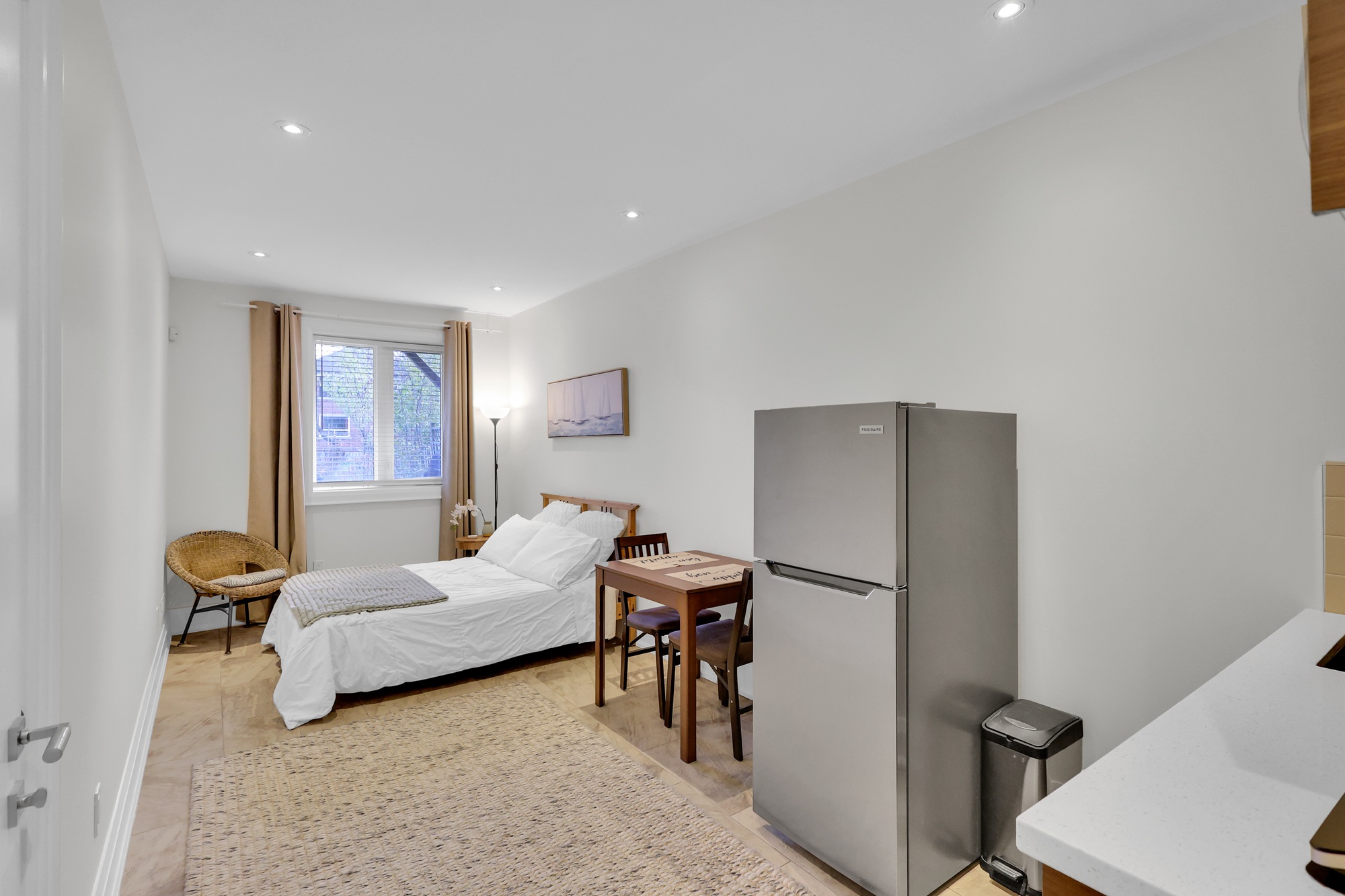 743 Glencarin Ave second basement studio unit with bed, dining set, fridge, tiled floors and window overlooking backyard.