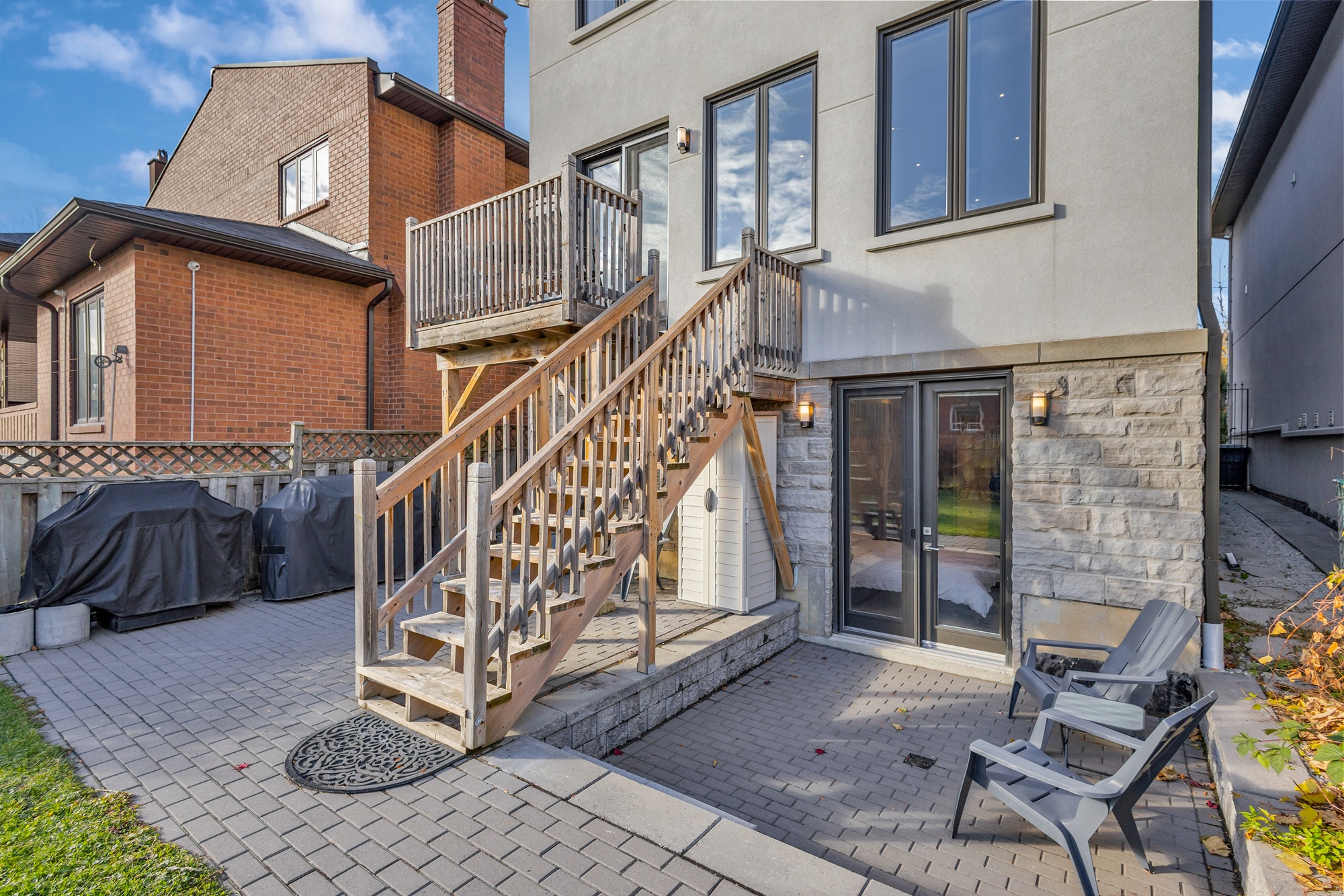 743 Glencairn Ave backyard with wooden deck, staircase and sunken stone patio with chairs.