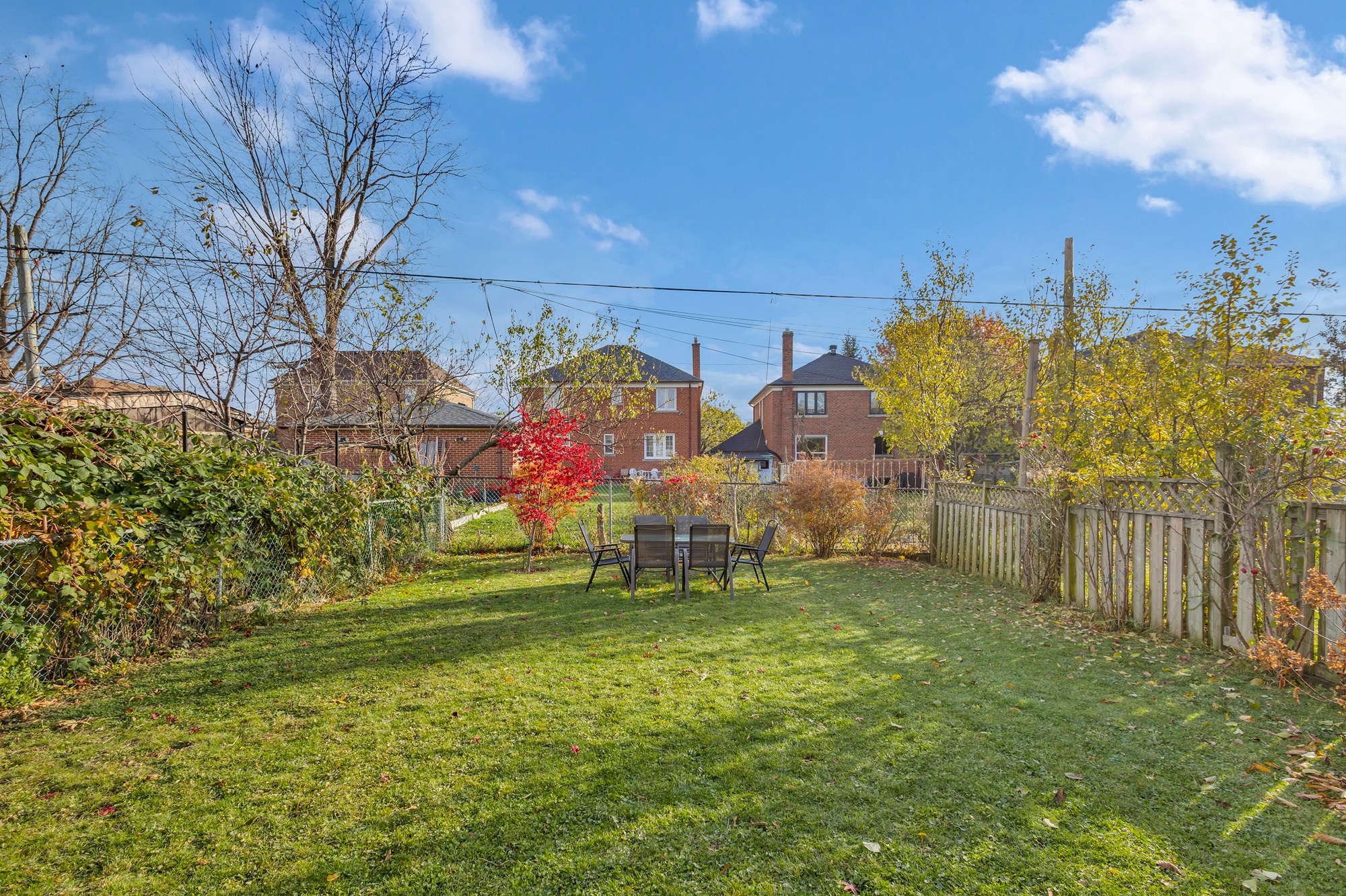 Large, lush fenced suburban backyard with patio furniture on lawn.