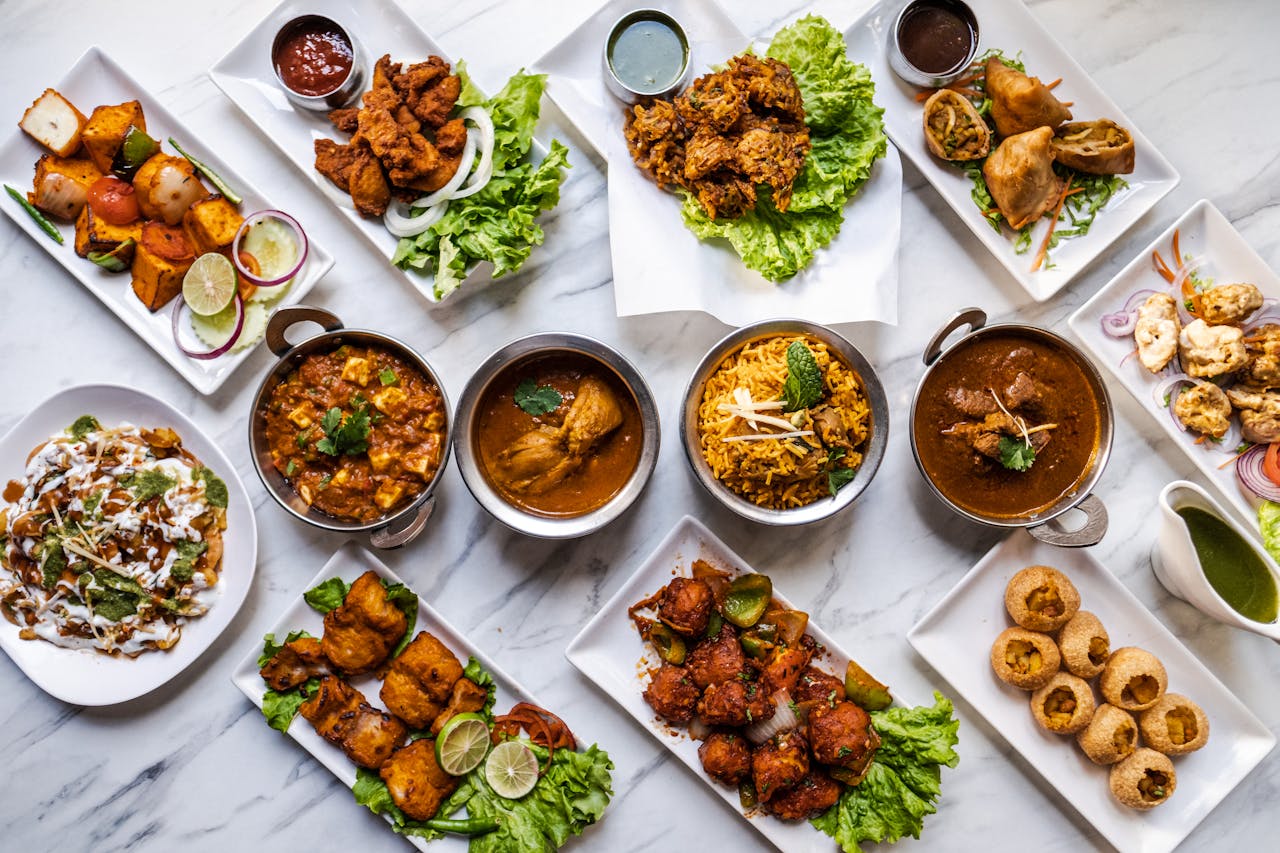 White table spread with Indian foods, including samosas, curries and meats.