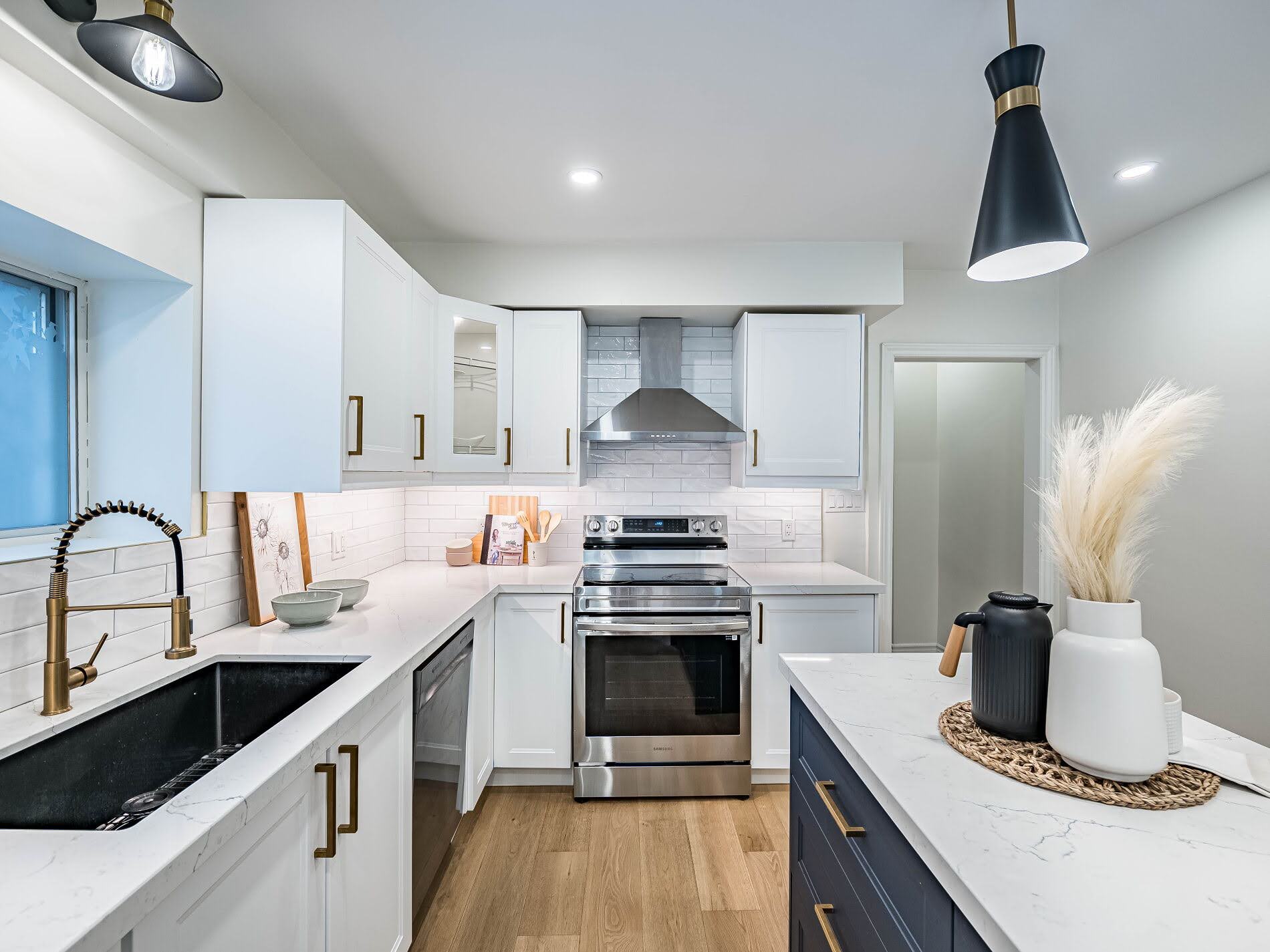 House kitchen with white cabinets, gold door handles, tiled back-splash, and valence lighting.